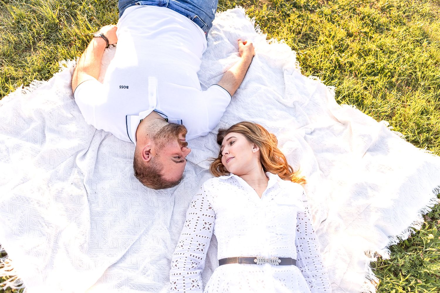 Couple in white outfits shares tender moments on grassy hillside.