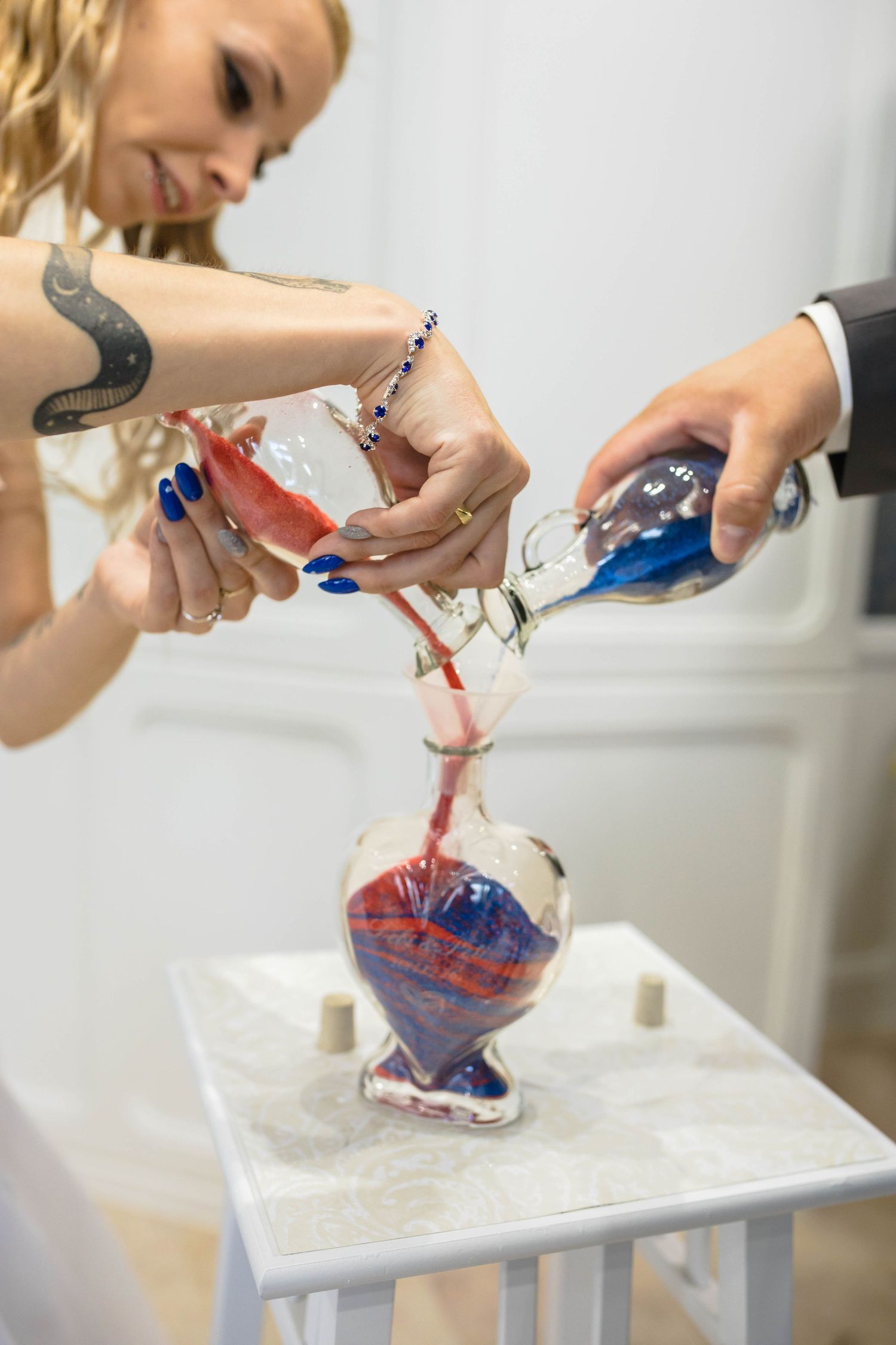 Hands pouring red and blue liquids into a glass container in a creative fluid art demonstration.