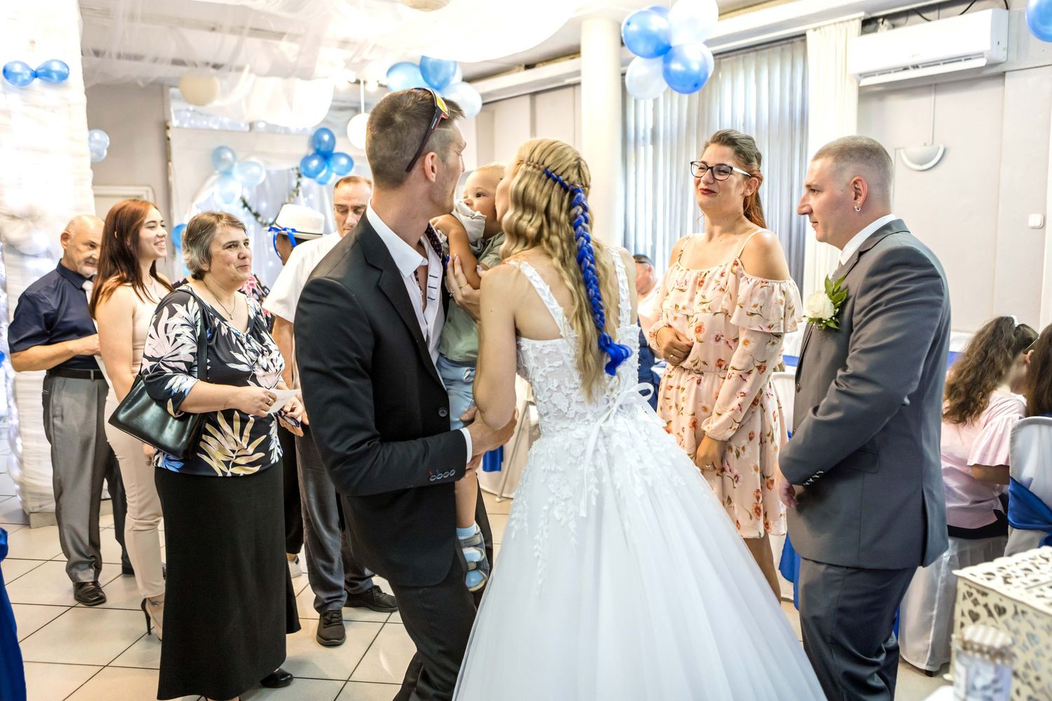 A wedding party celebrates with blue balloons and confetti during an outdoor reception.
