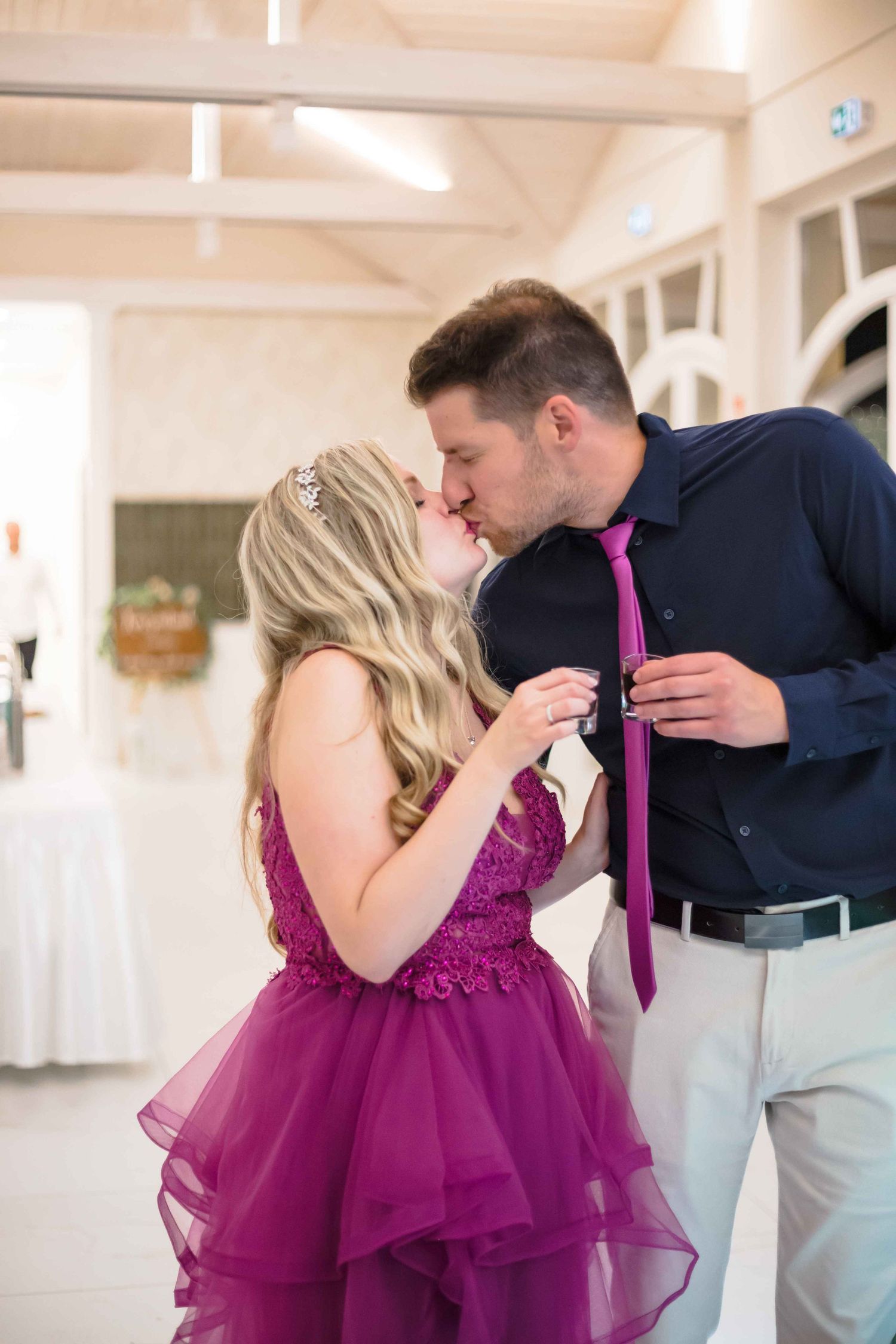 A couple shares an intimate moment in a bright indoor setting, with the woman wearing a vibrant magenta tulle gown.