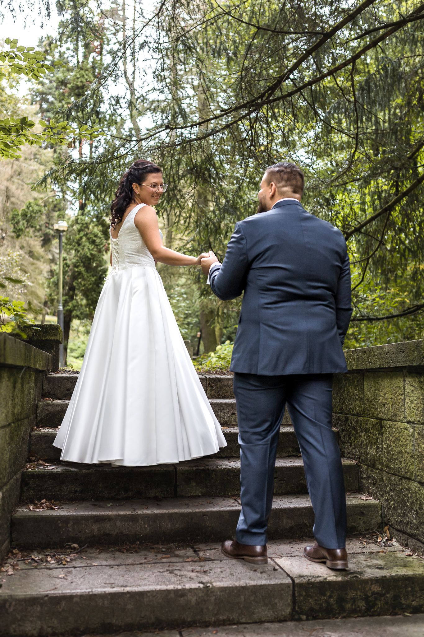 A couple in wedding attire playfully poses on stone steps surrounded by greenery in a series of candid moments.