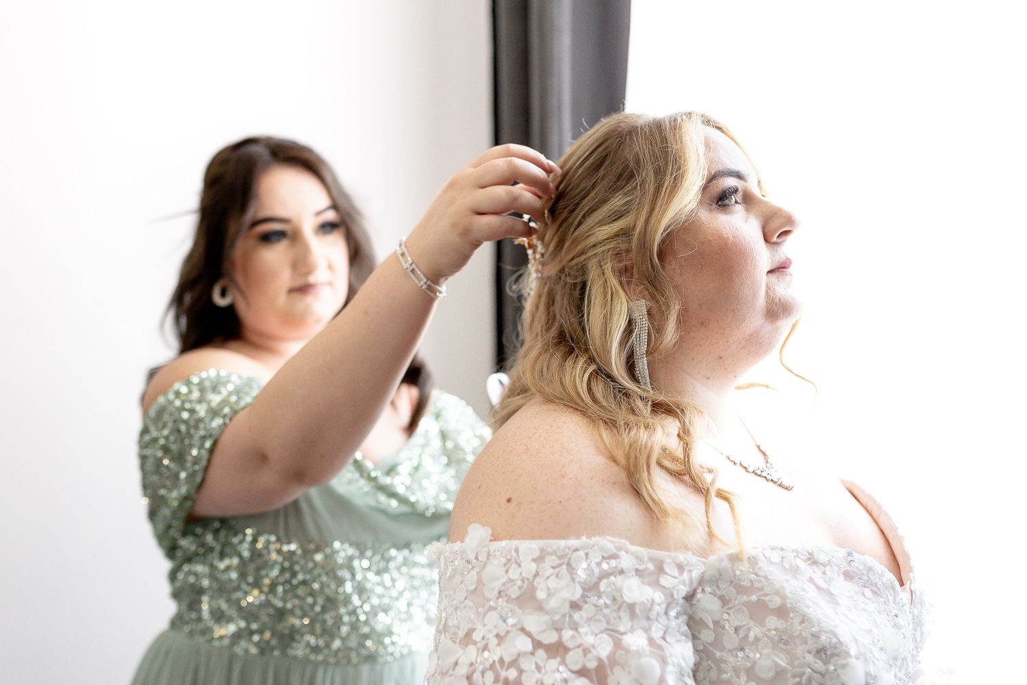 A group of bridesmaids in mint green dresses help the bride get ready before the wedding ceremony.