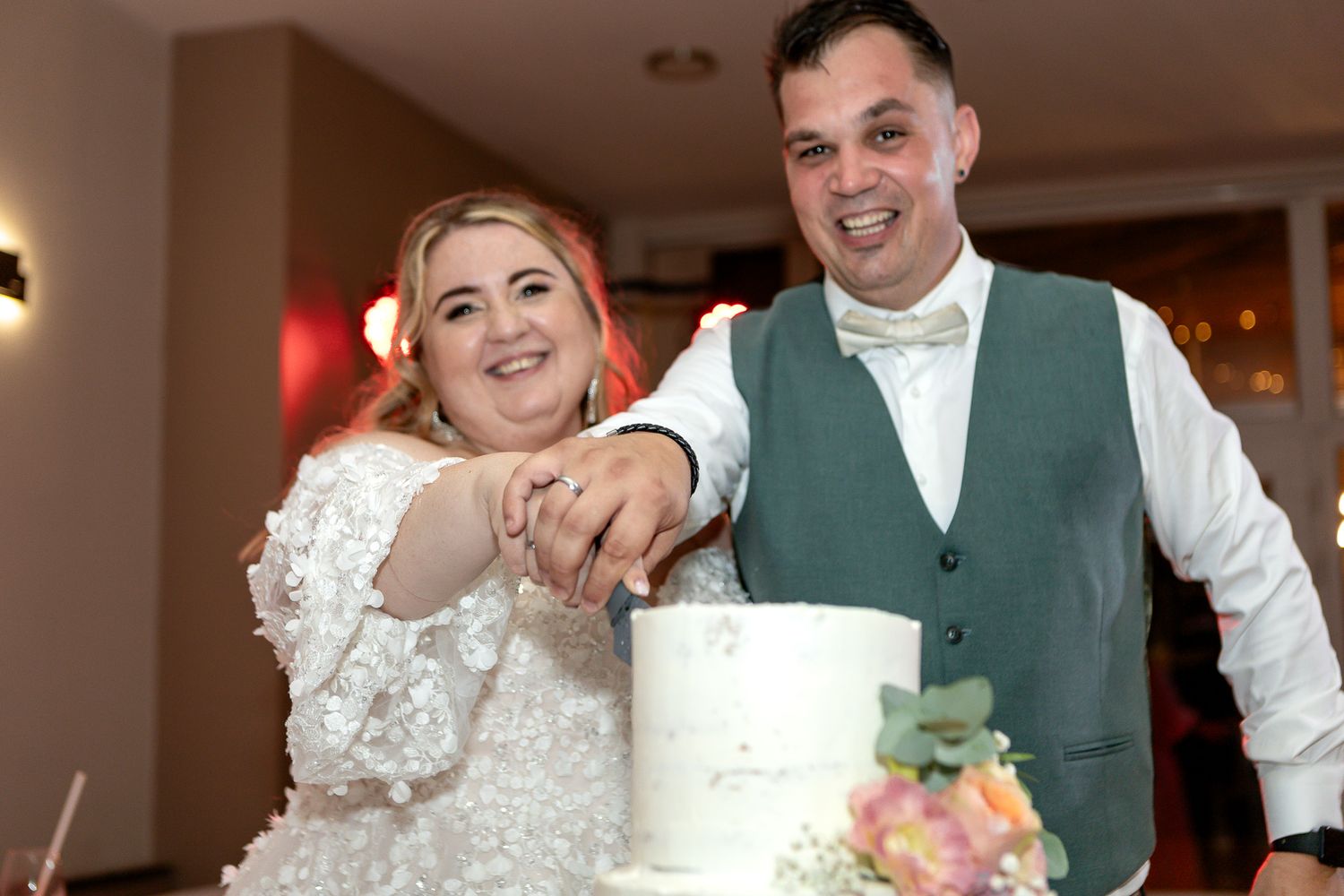 Wedding couple sharing a playful moment while cutting their wedding cake at an indoor reception venue.