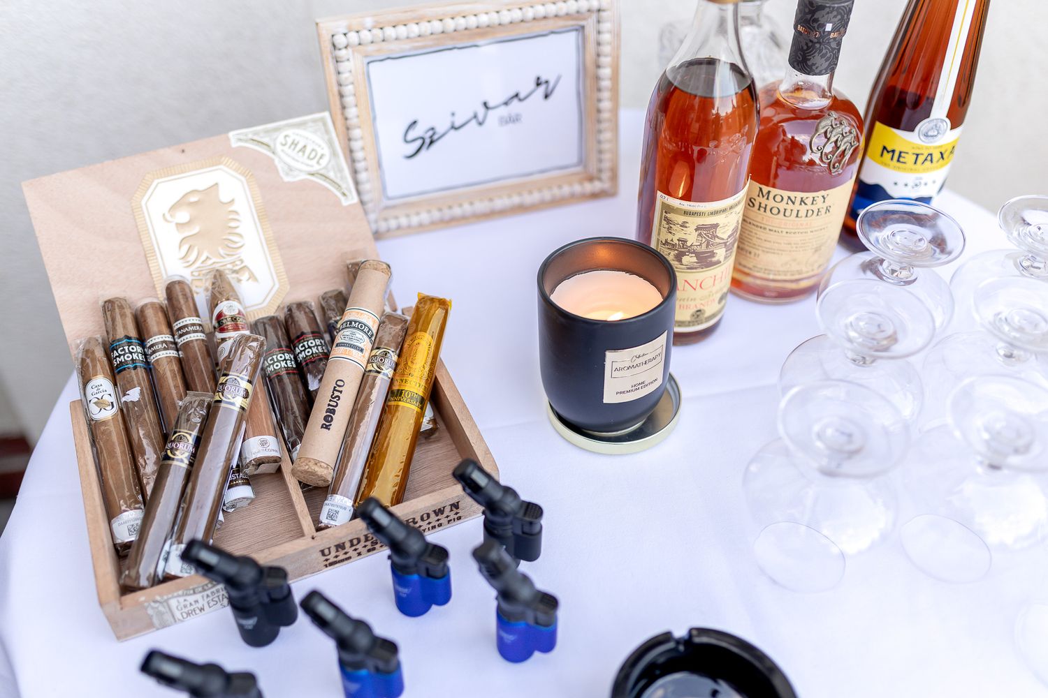 A collection of cigars, whiskey bottles, candles and accessories arranged on a white surface for a luxury lifestyle setup.