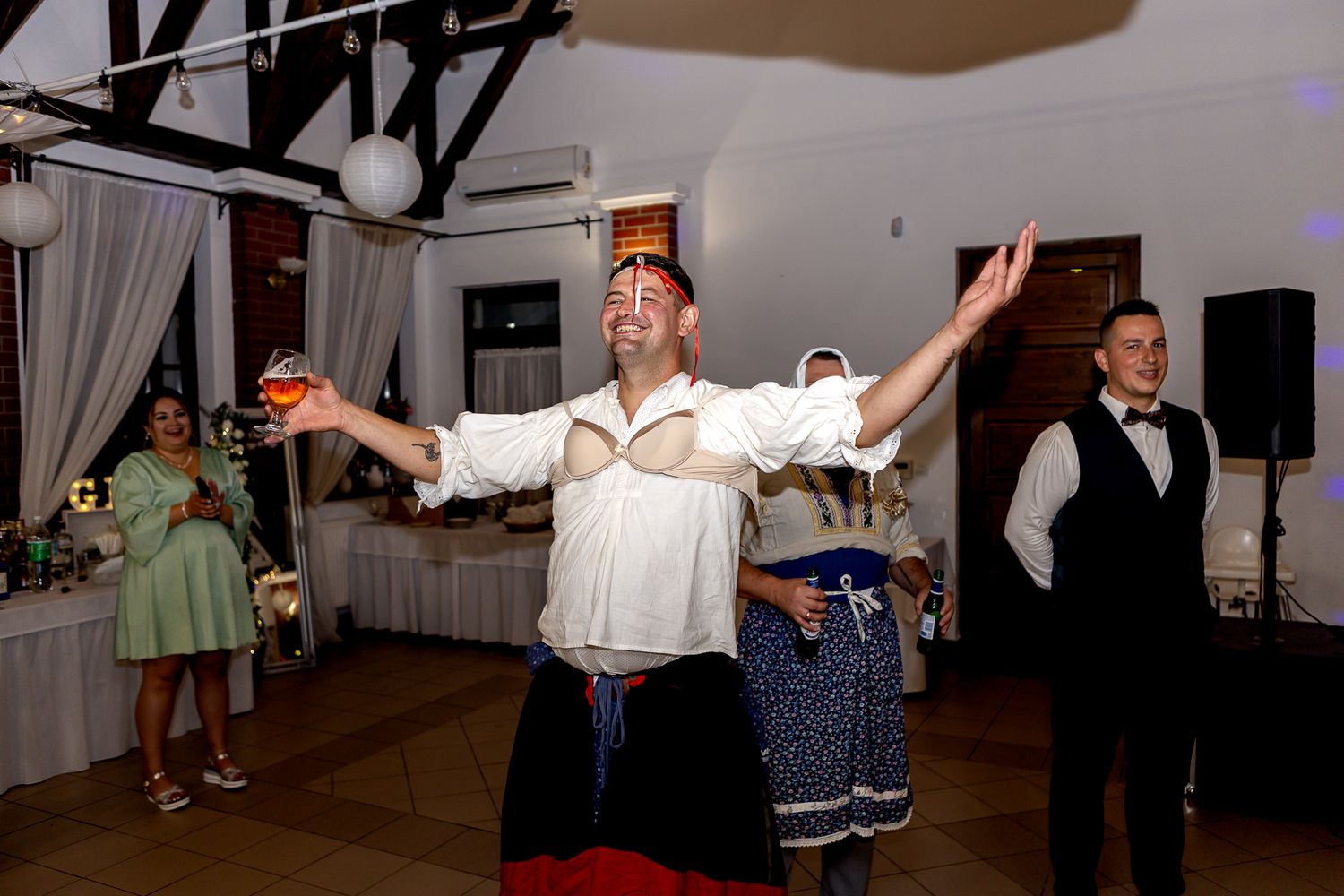 Wedding guests dancing and celebrating on a dance floor at an indoor reception venue with white decor.