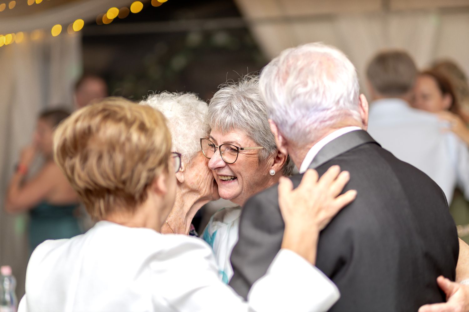 A group of people dancing and celebrating at a wedding reception with blurred bokeh lights in the background.
