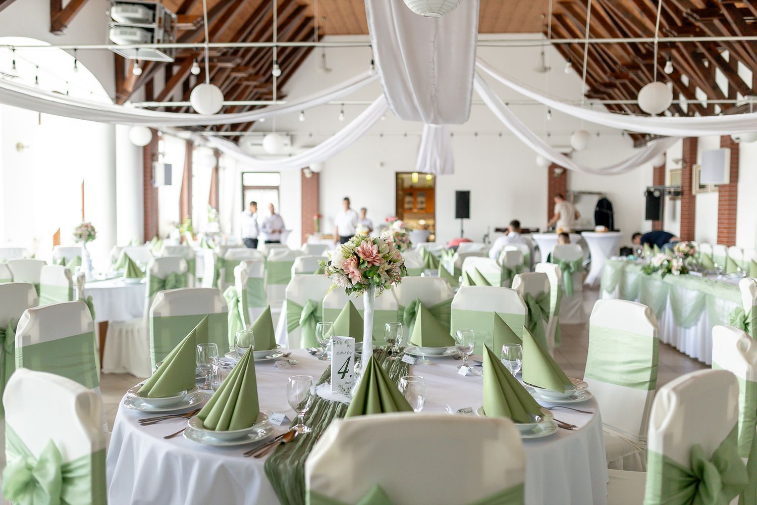 Elegant wedding reception venue with white draping and mint green accents features long banquet tables and rustic beams.