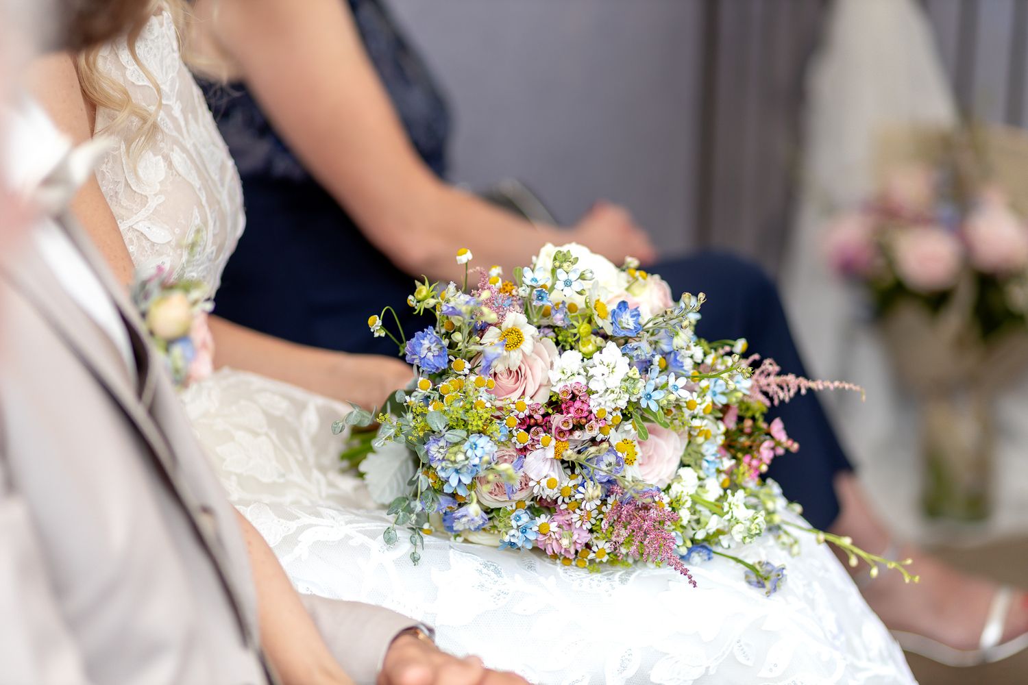 A wedding bouquet with delicate blue and white wildflowers held by someone wearing a white lace dress.
