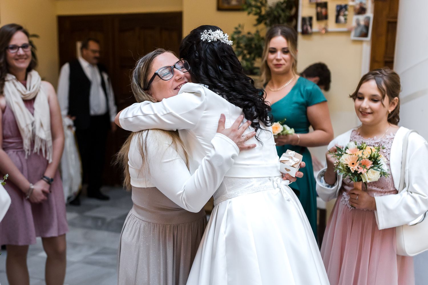 Emotional wedding moment captured as people embrace while others look on with bouquets in hand.