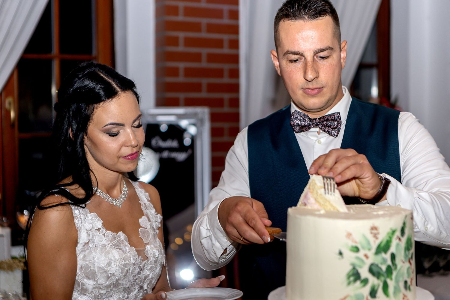 Newlywed couple cuts their elegant white and green wedding cake together at their reception.