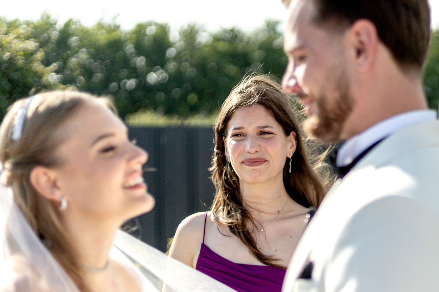 Wedding party members share candid moments during outdoor ceremony.