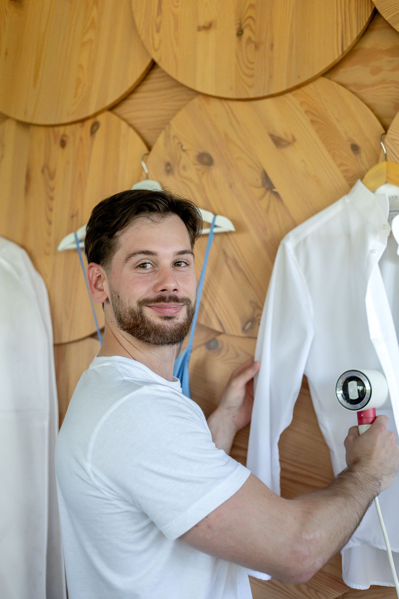 Person in white shirt organizing clothing on hangers against wooden wall.