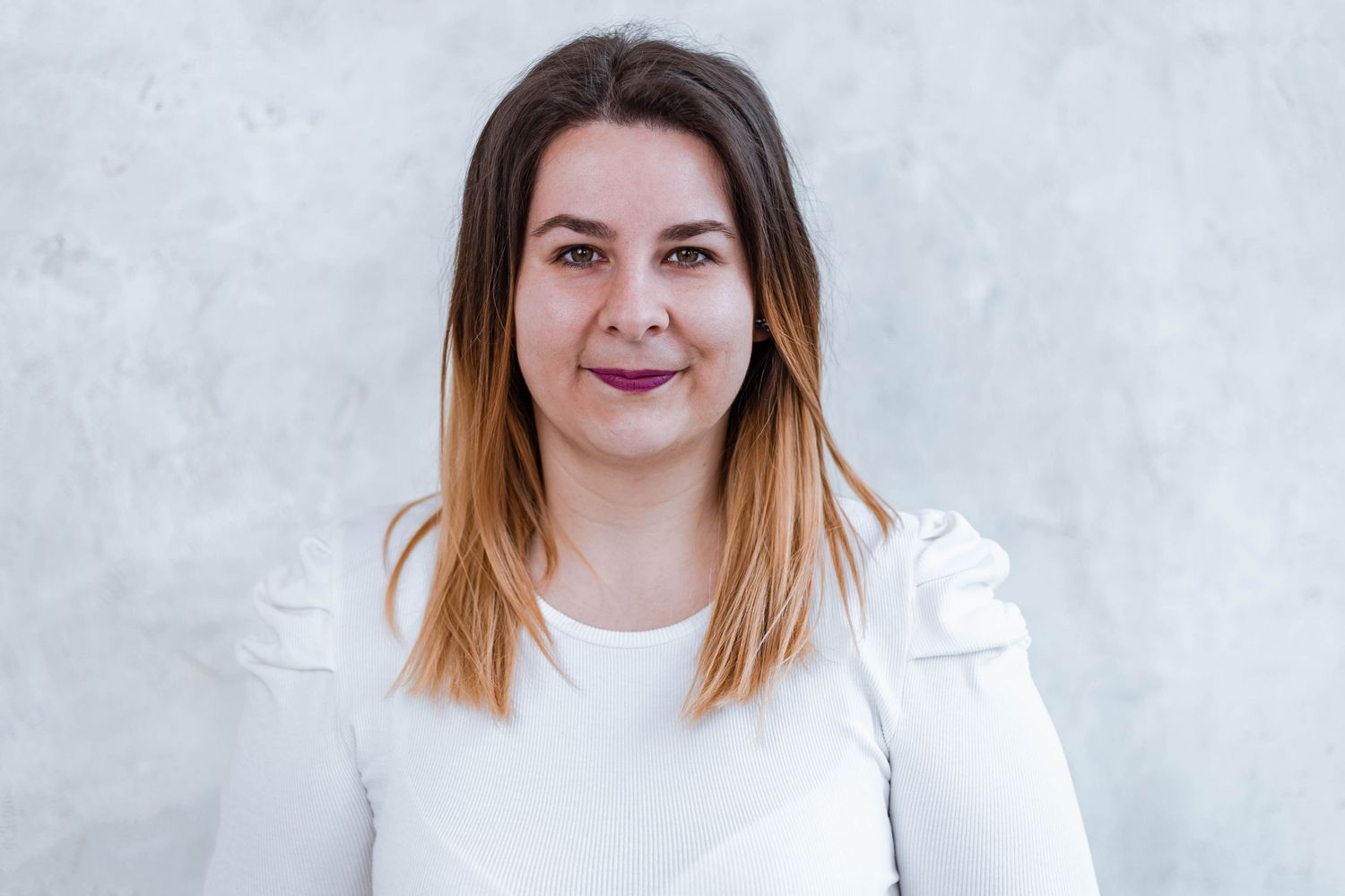 Woman with ombre hair poses confidently in white outfit against light background.