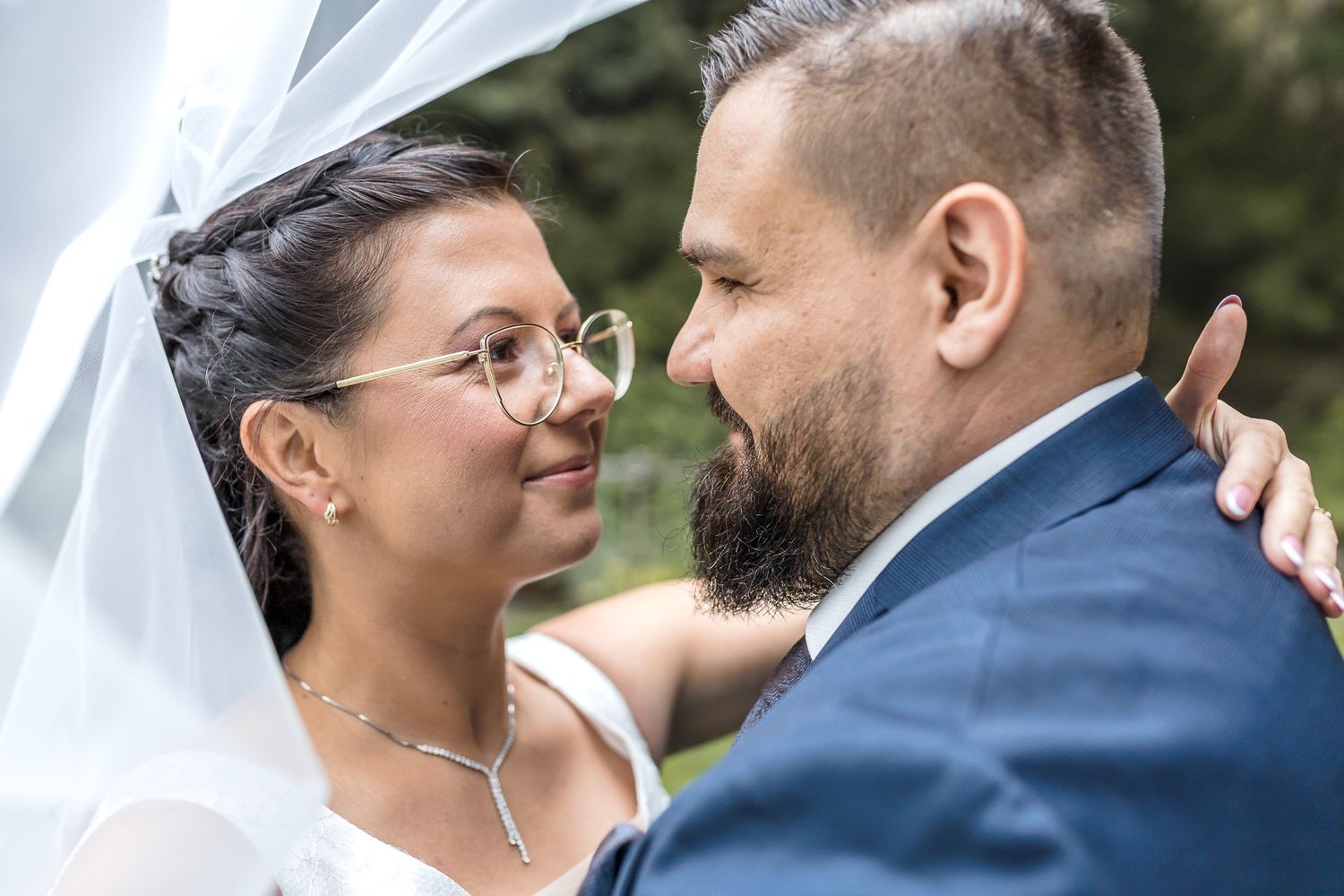 Tender wedding moment between couple in formal attire with bride wearing glasses.