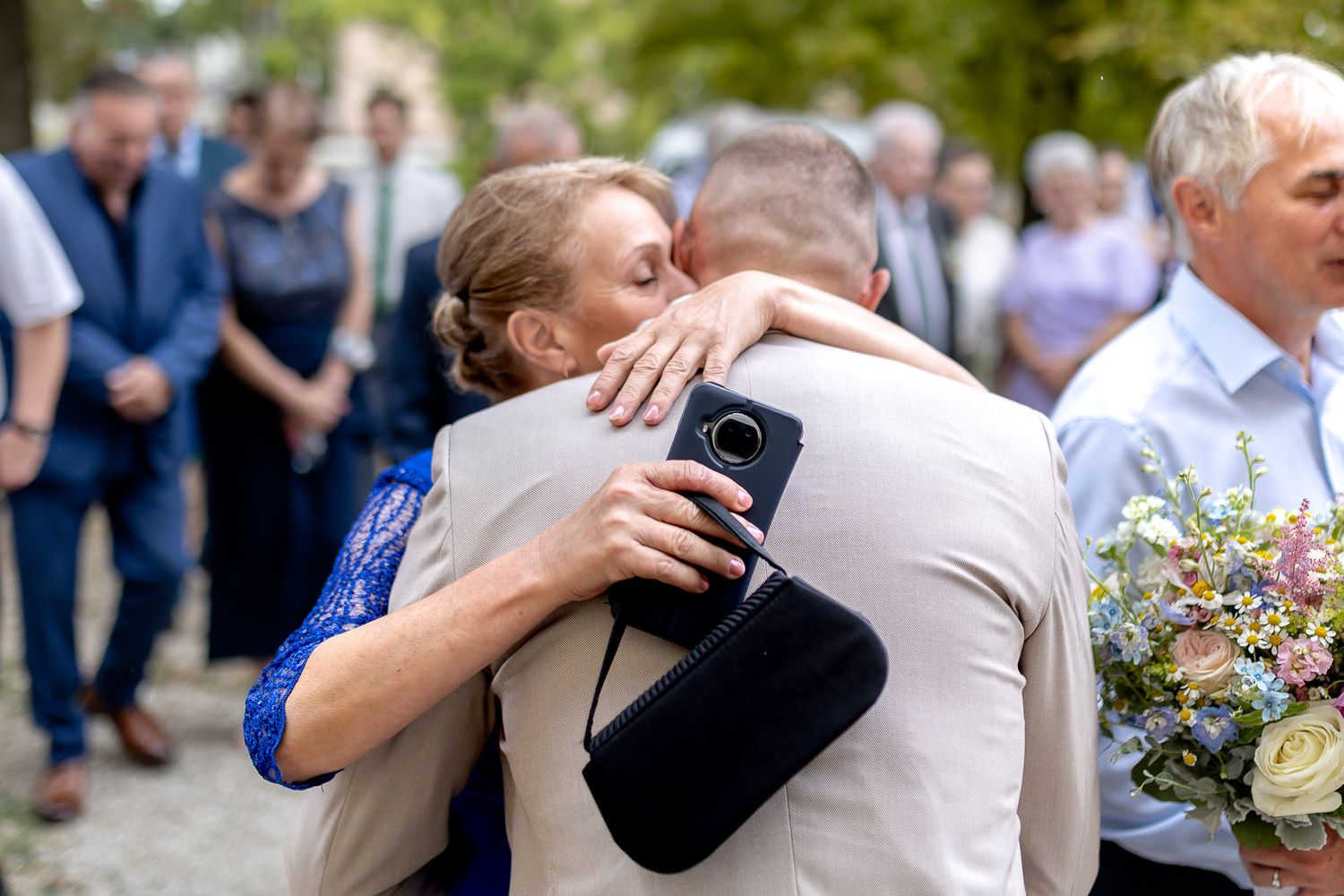 People hugging and embracing at a wedding celebration with flowers and guests in the background.