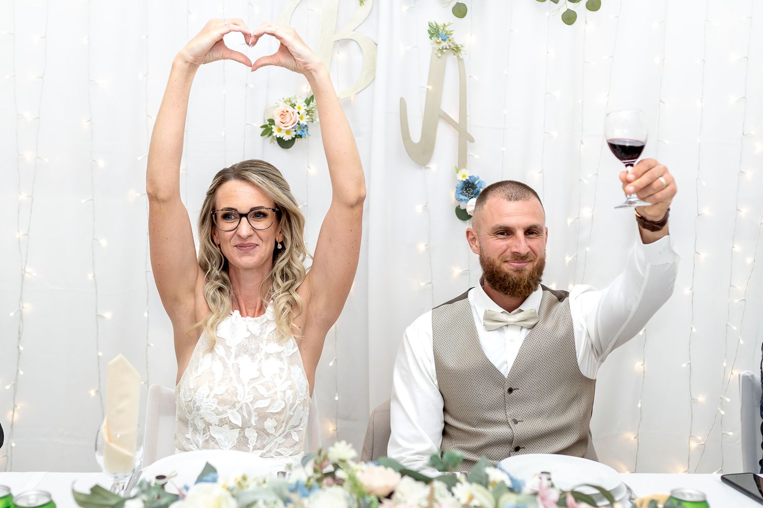 Wedding guests make heart shapes with their hands while holding wine glasses during a celebratory toast.