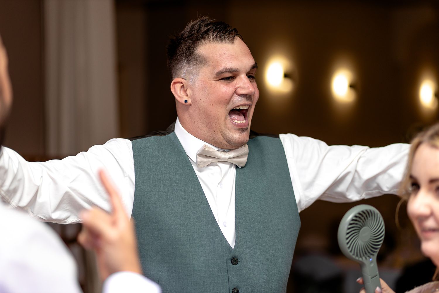 Wedding guests dancing and celebrating on a dance floor with festive lighting in the background.