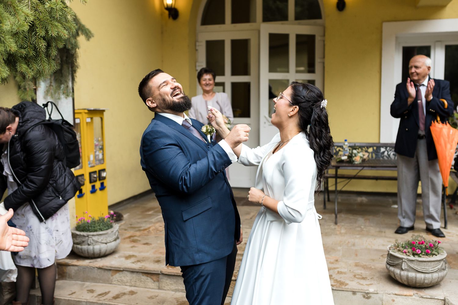 A joyful couple shares a candid moment of laughter during their outdoor wedding celebration at a yellow villa.