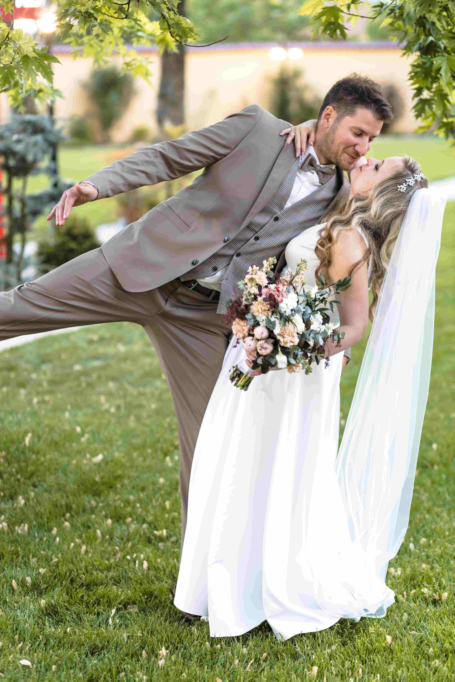 Wedding party member in tan suit performs funny falling pose sequence on grassy lawn during outdoor photo session.