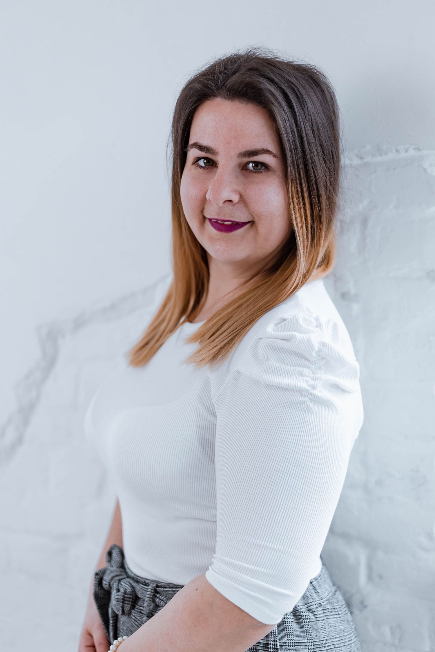 Woman with ombre bob hairstyle smiles while wearing white top in bright room.