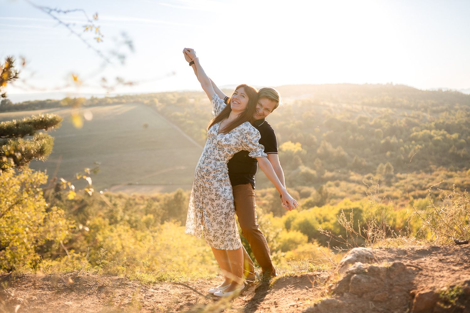 Couple sharing intimate moment on mountain overlook during sunset.