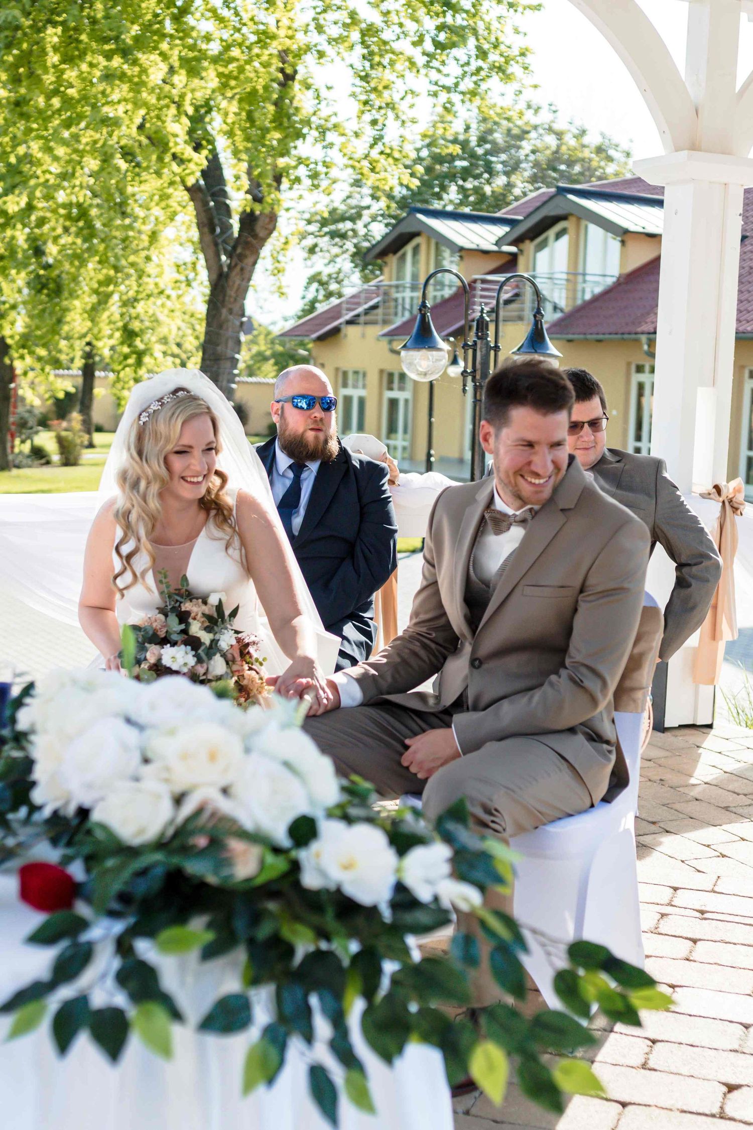 Joyful moment captured during an outdoor wedding ceremony with beautiful floral arrangements on a sunny day.