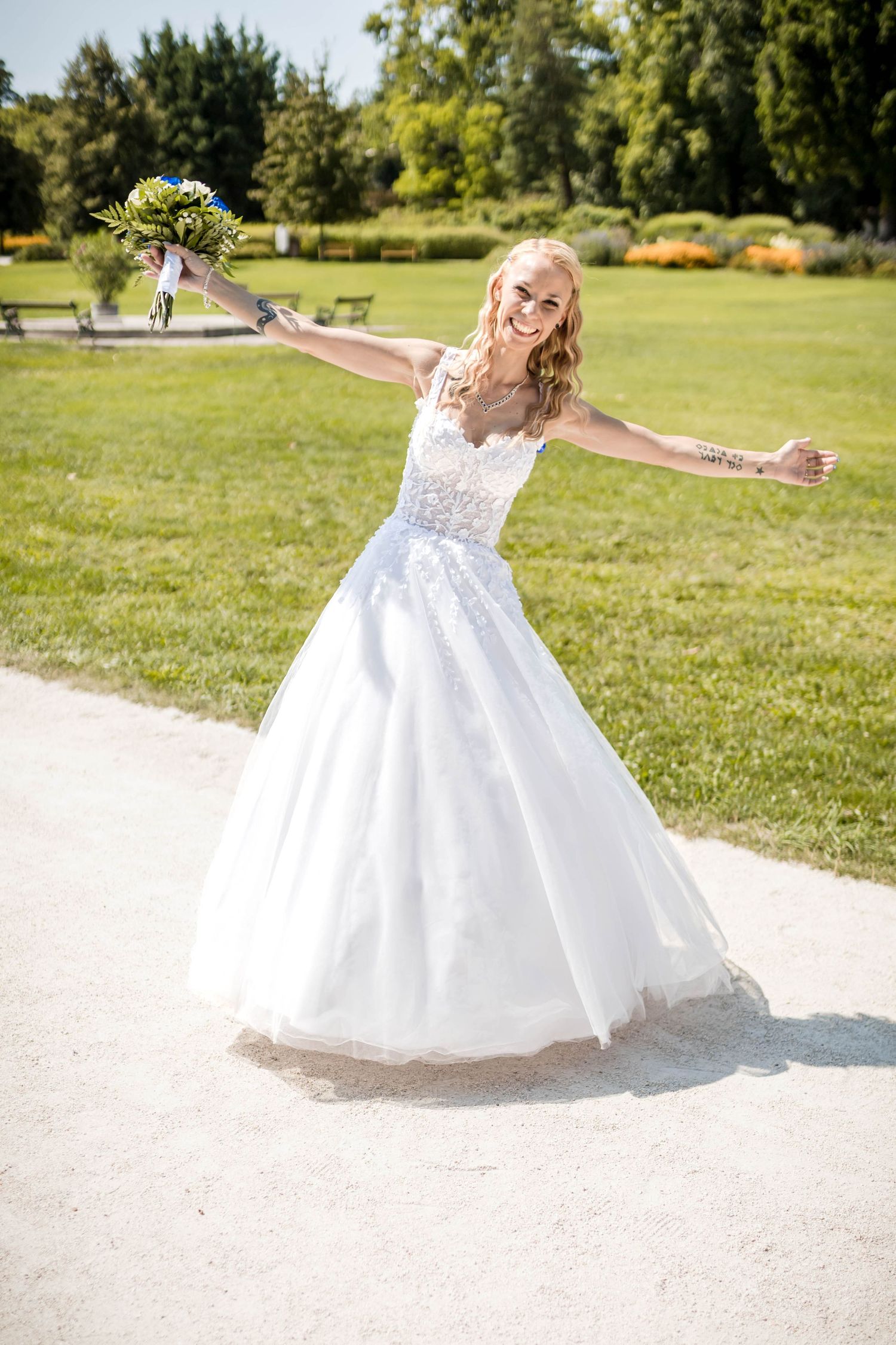 A young dancer in a flowing white dress twirls joyfully on a paved path surrounded by green grass and trees.