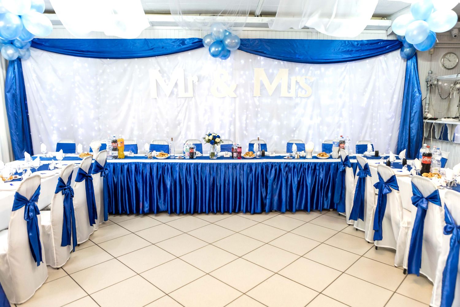 Elegant wedding reception venue decorated in royal blue and white with tables arranged in a U-shape formation.