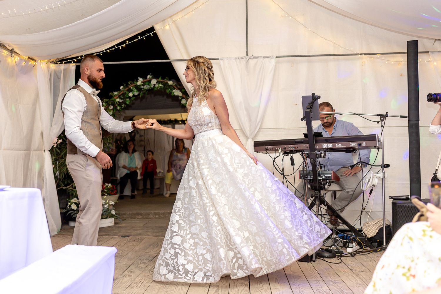 Wedding guests dance and celebrate under a white tent decorated with string lights during an evening reception.