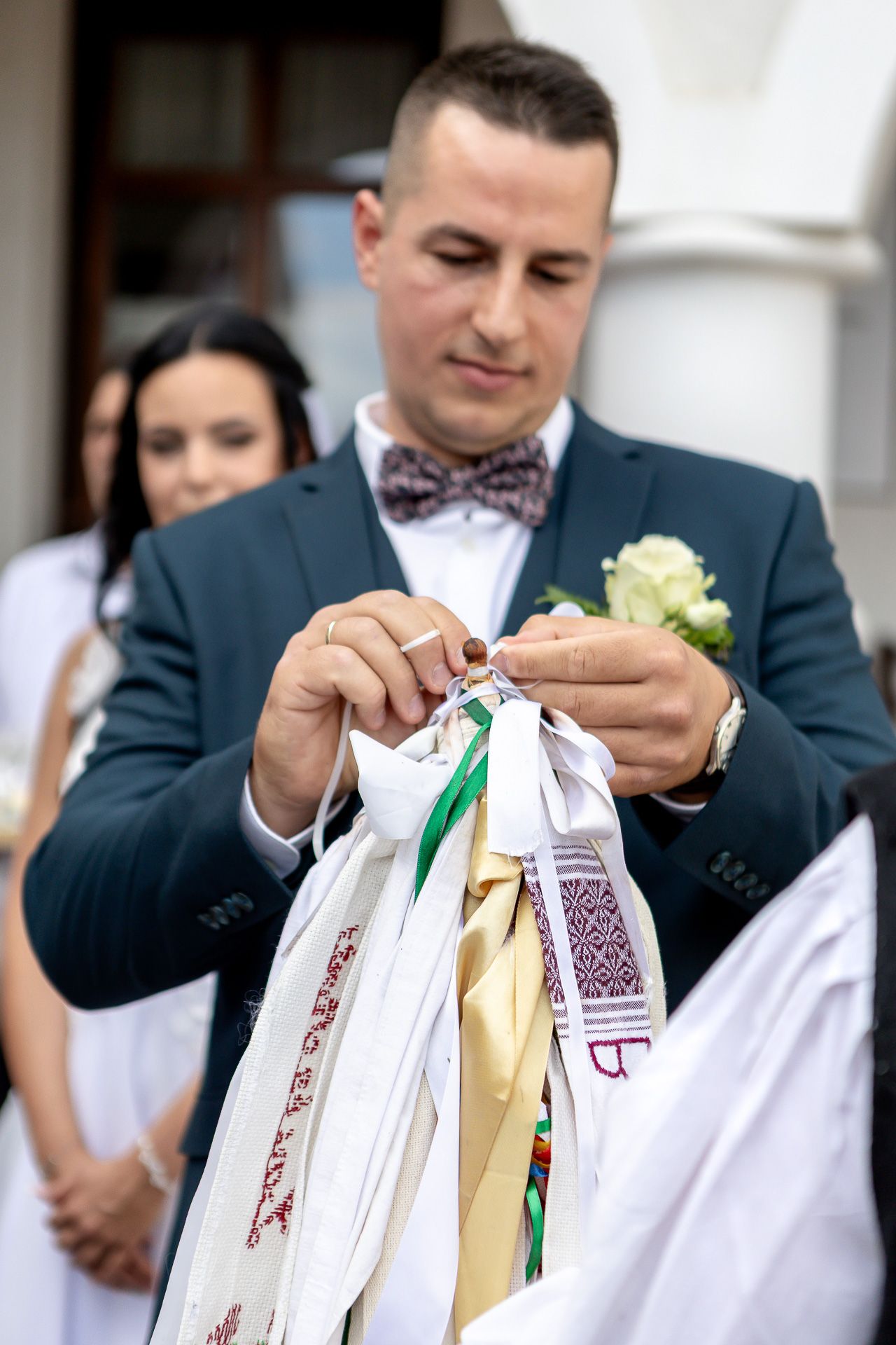 Wedding guests tie colorful ribbons and well wishes onto traditional wedding wands at an outdoor celebration.