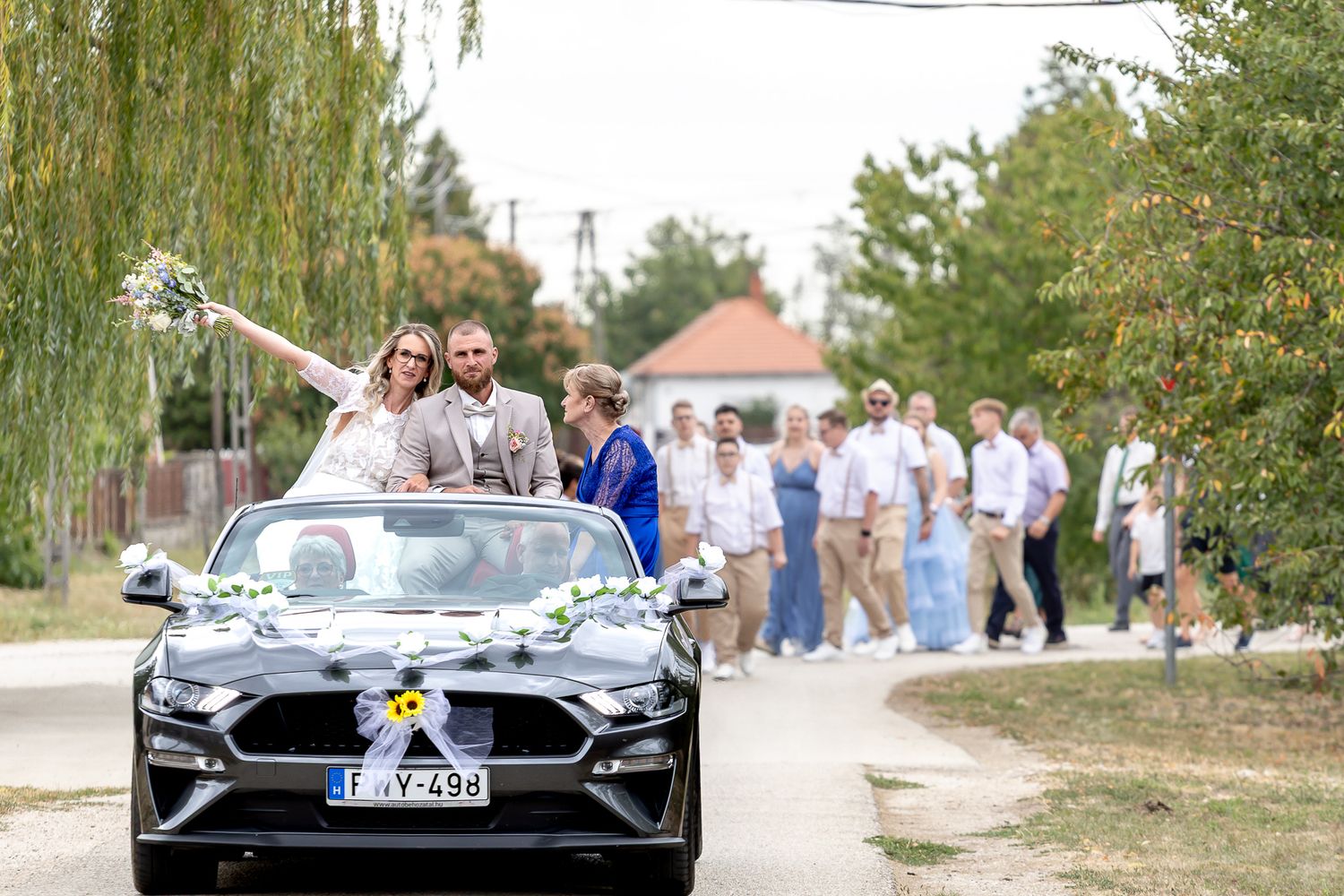 A sleek black Porsche sports car parked on a dirt road with people gathering in the background.