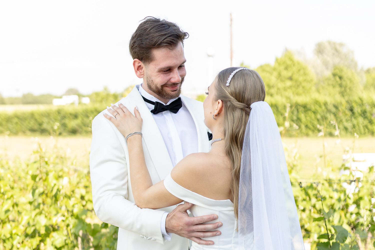 A newlywed couple embraces in a sunny vineyard setting.