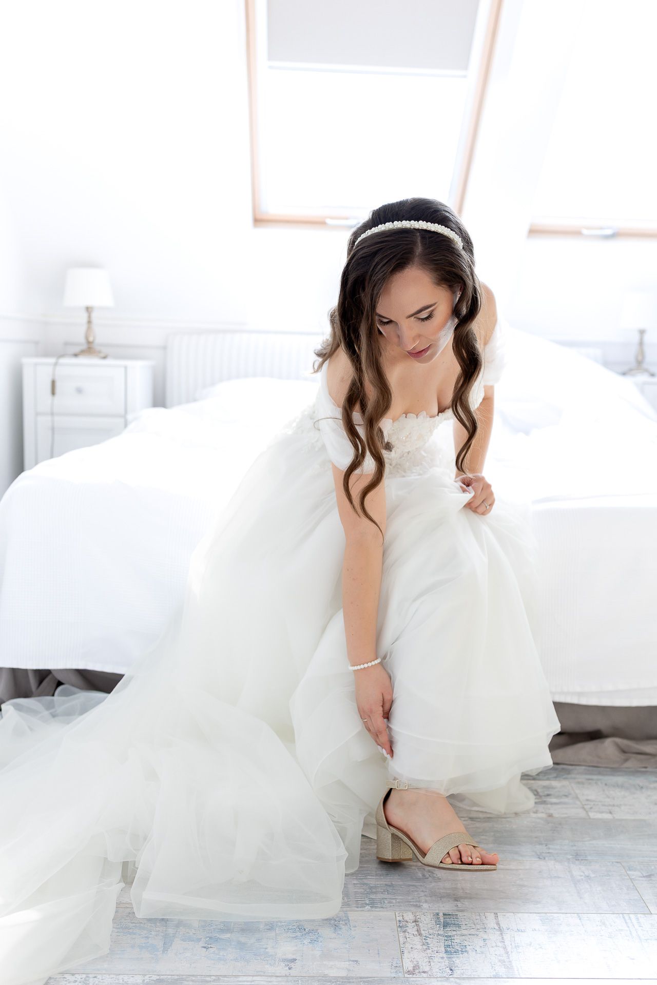 A flowing white wedding dress with delicate details is showcased in a bright, minimalist indoor setting.
