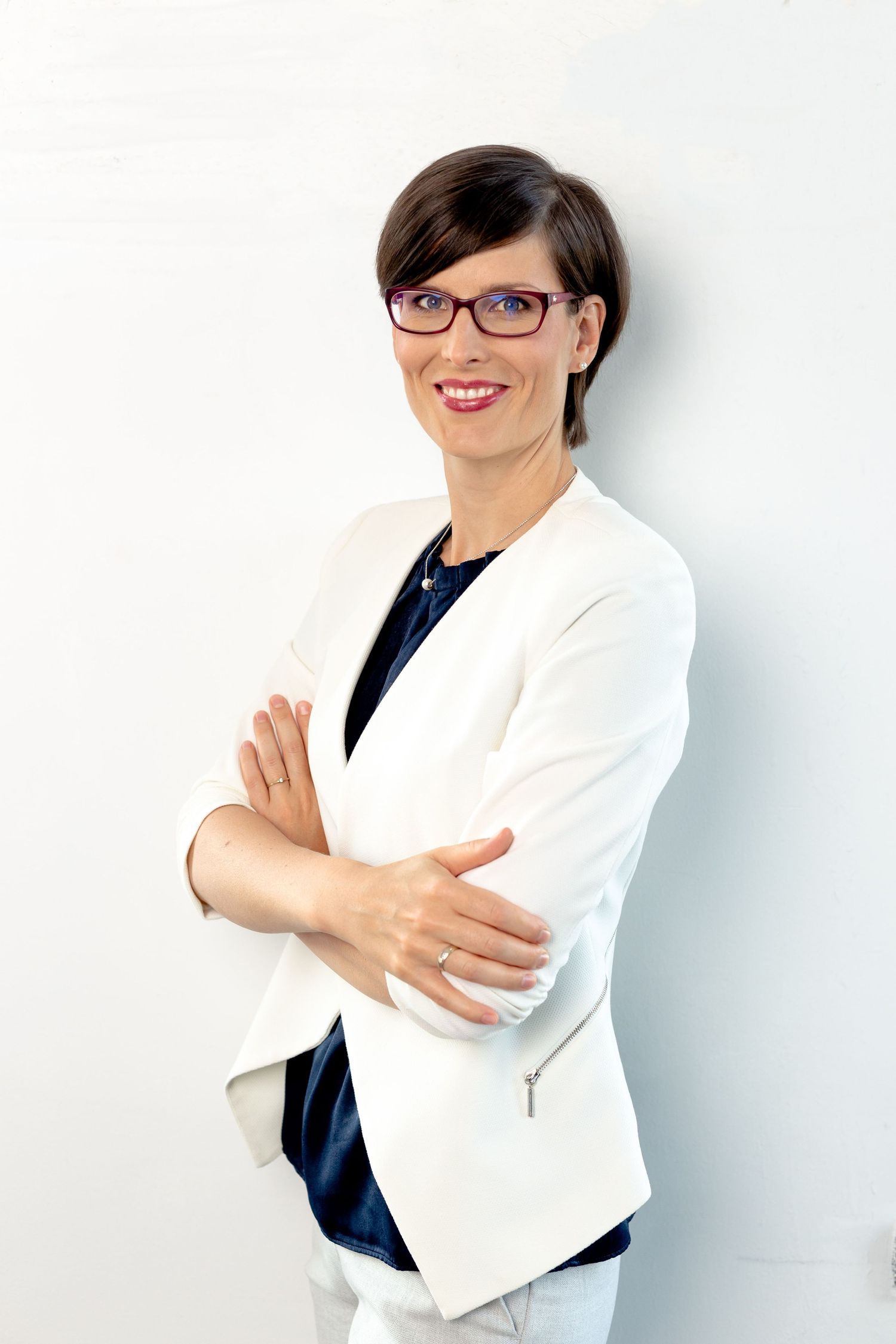 Professional business portrait against white wall wearing crisp white blazer and glasses.