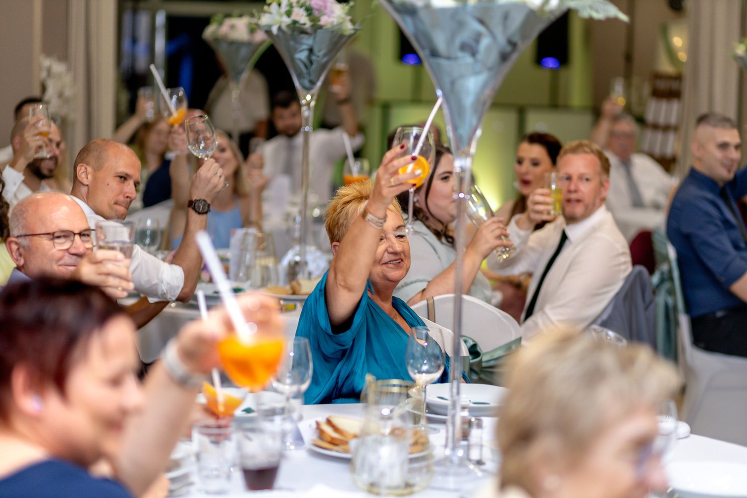 Wedding guests raise their glasses in a celebratory toast during an elegant indoor reception.