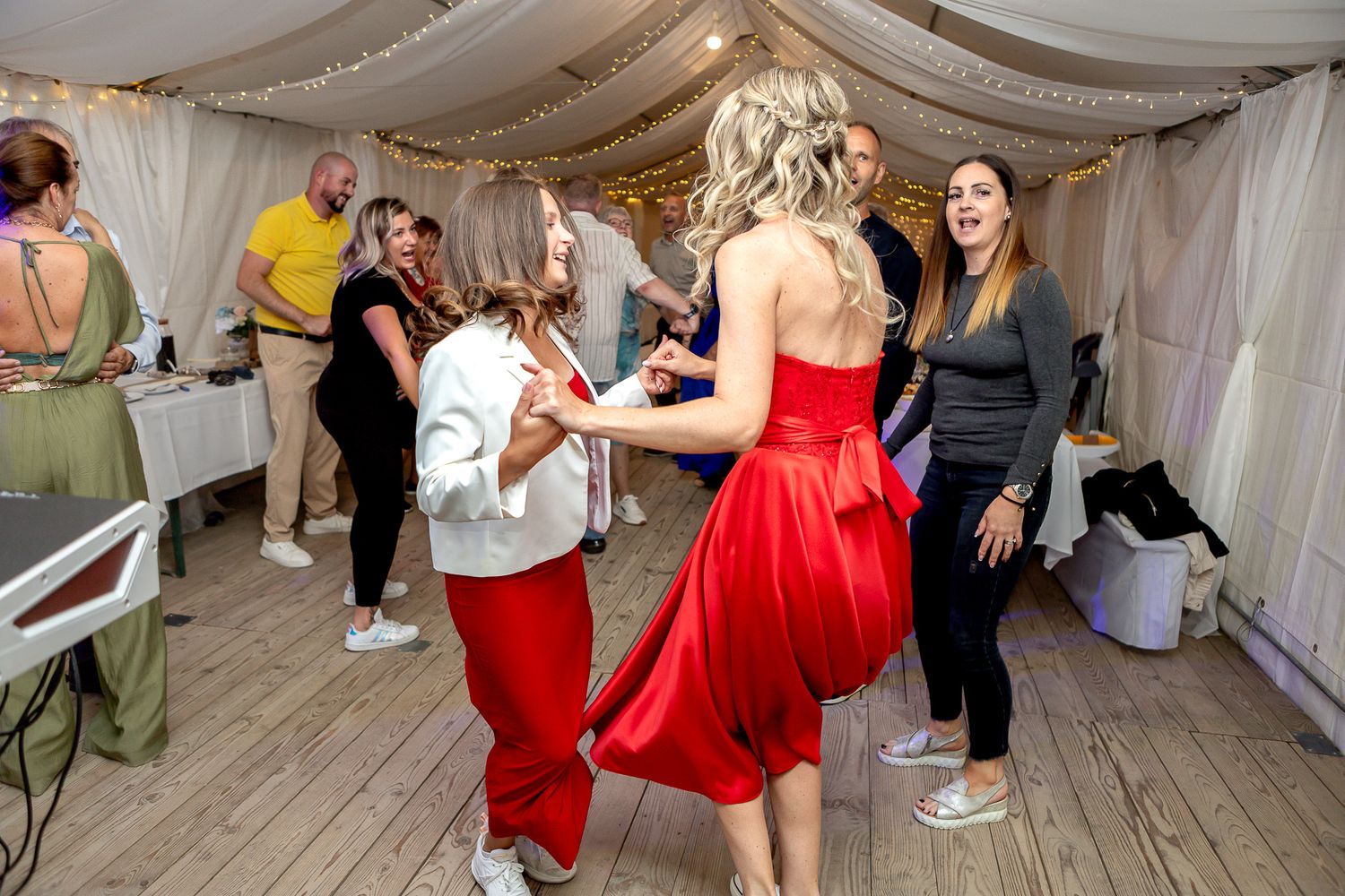 People dancing and celebrating at a wedding reception under white draped fabric decor.