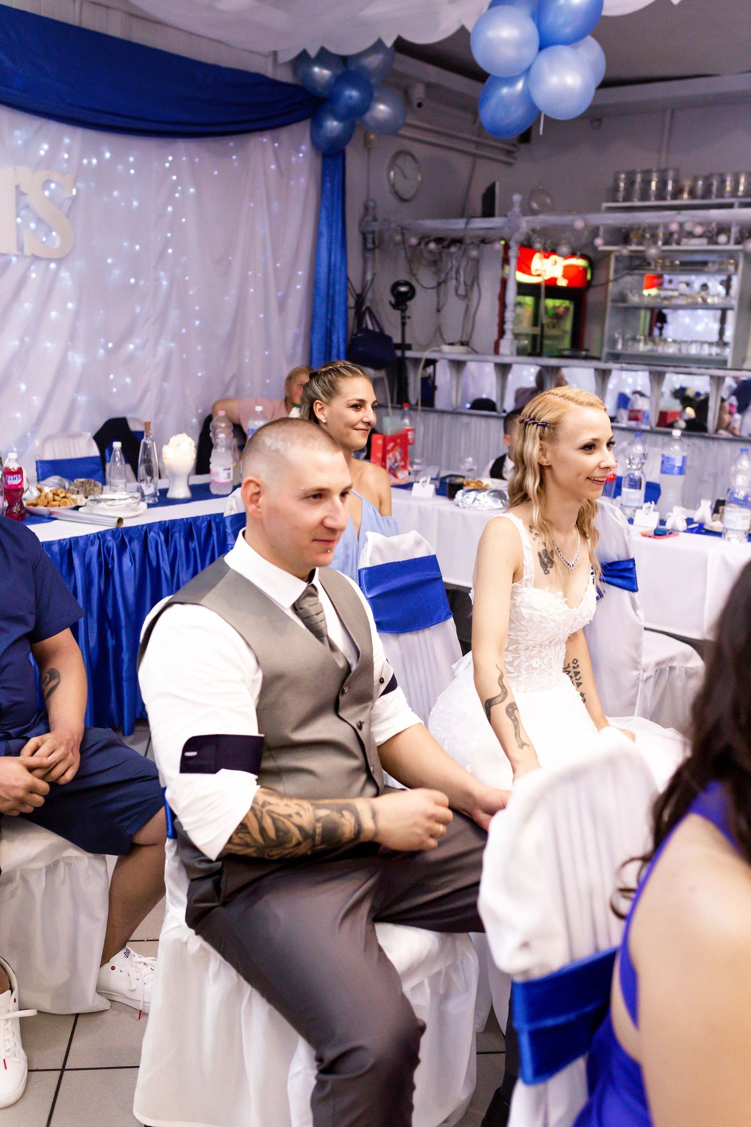 Wedding reception guests in white and blue decor celebrate at tables with festive balloon decorations.