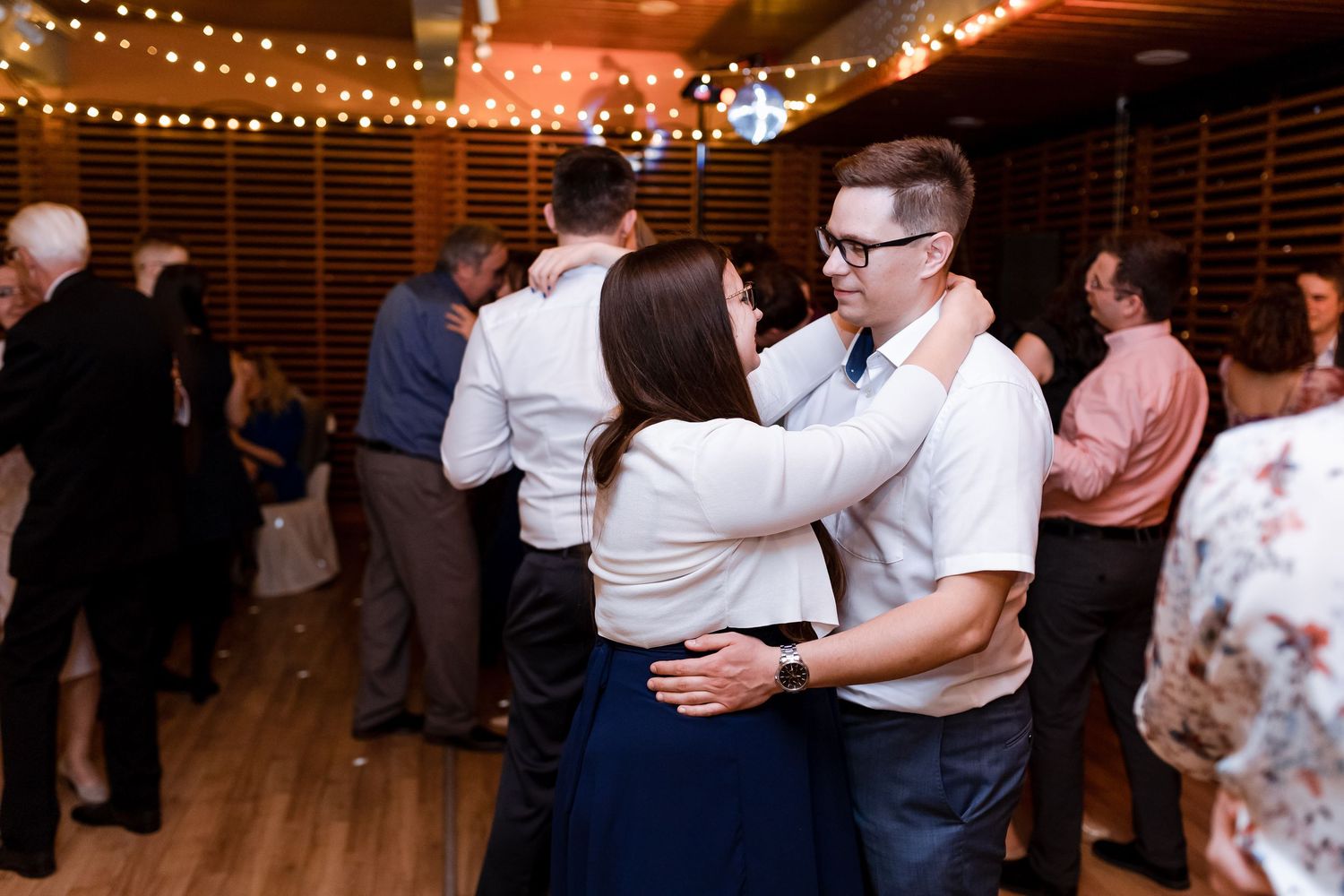 Couples dance together at a rustic wedding reception venue decorated with warm string lights.