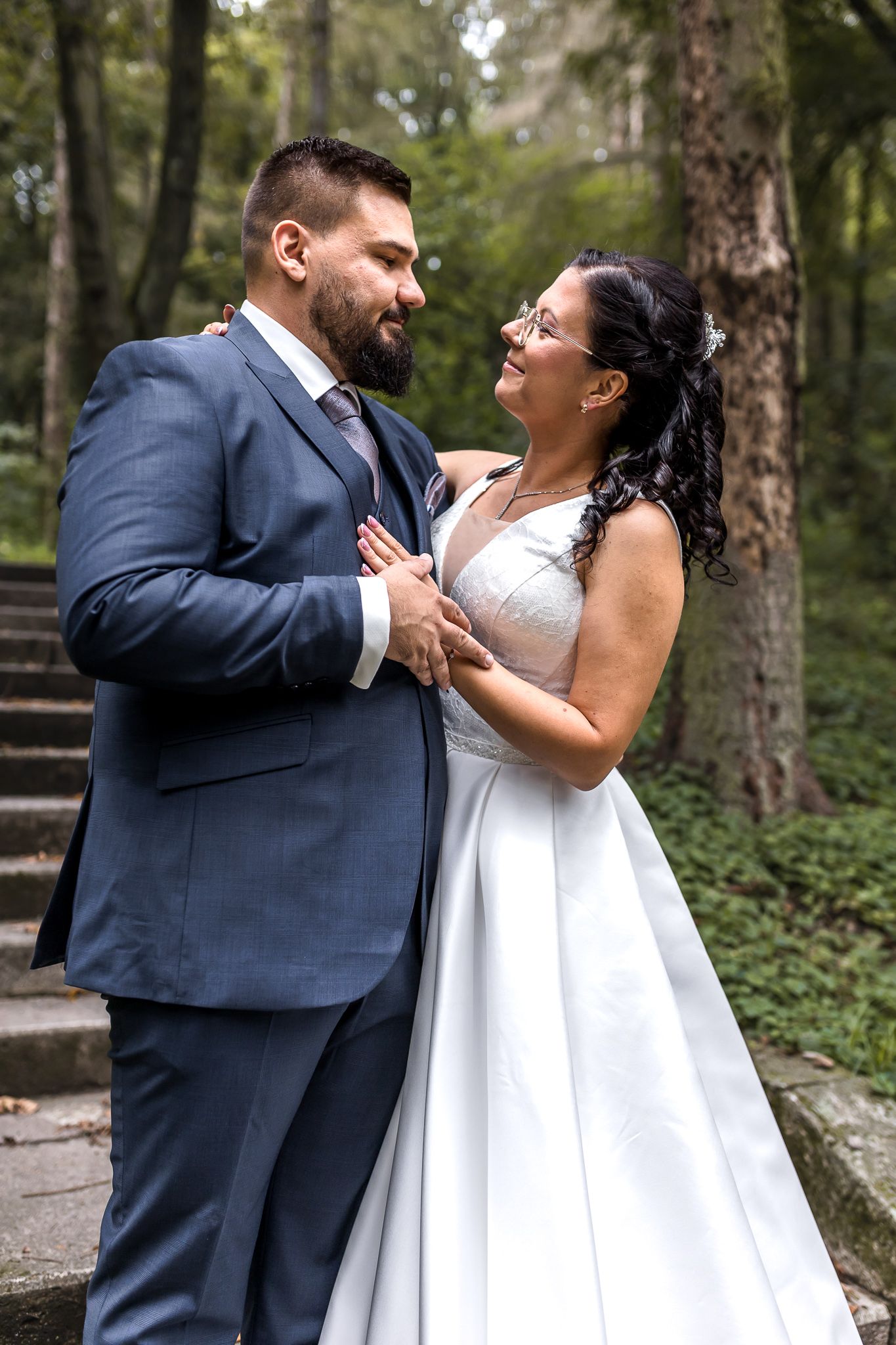 A couple in wedding attire shares a joyful moment together in a wooded outdoor setting.