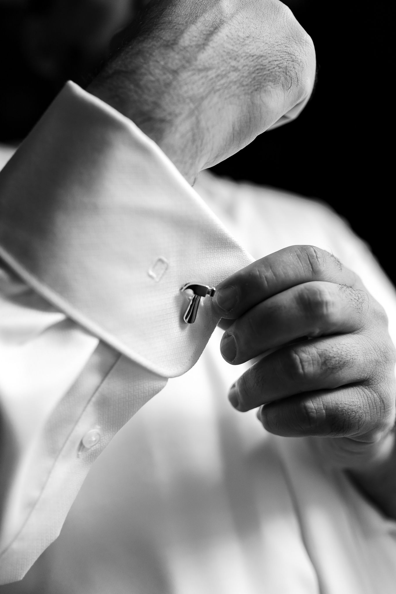 Close-up black and white image of hands adjusting a white dress shirt cuff in elegant lighting.