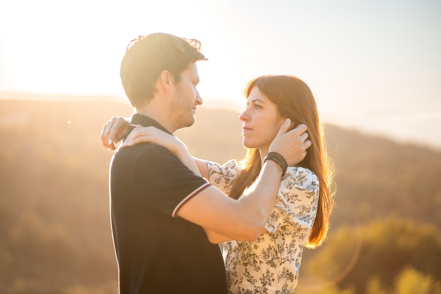 Couple dancing and embracing during golden hour on hilltop.
