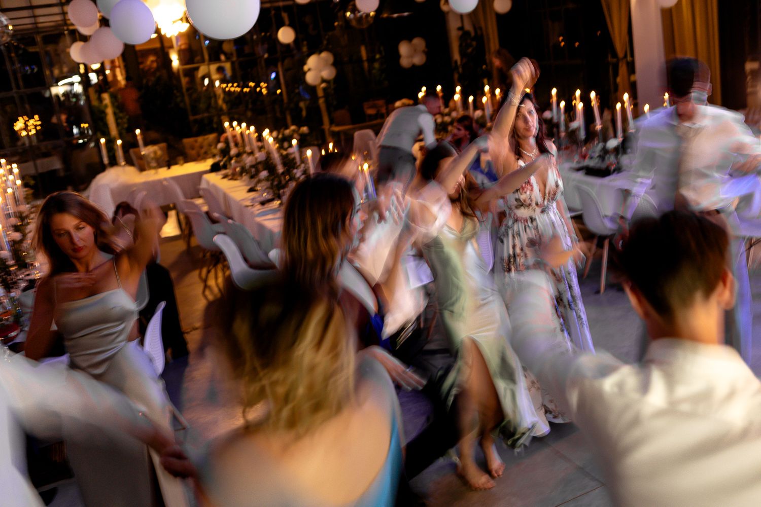 Blurred motion shot of people dancing at a festive celebration with hanging lights.