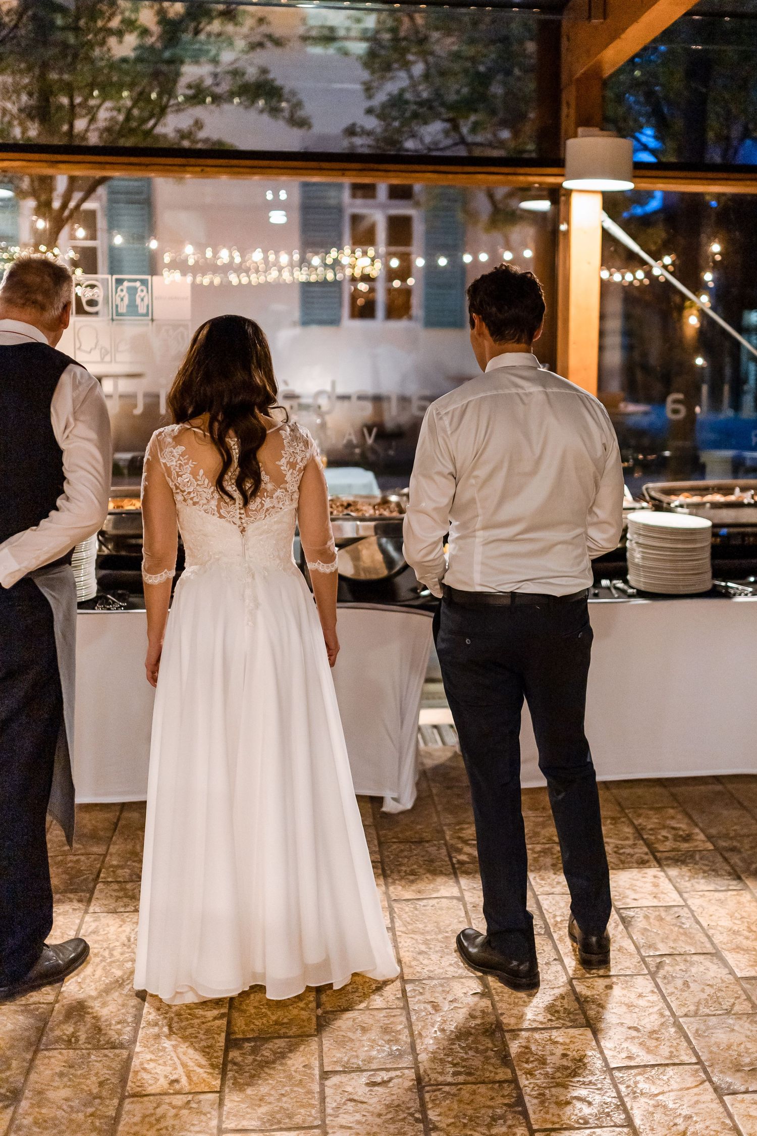 Wedding guests dance together on a stone patio under twinkling string lights at an outdoor evening reception.