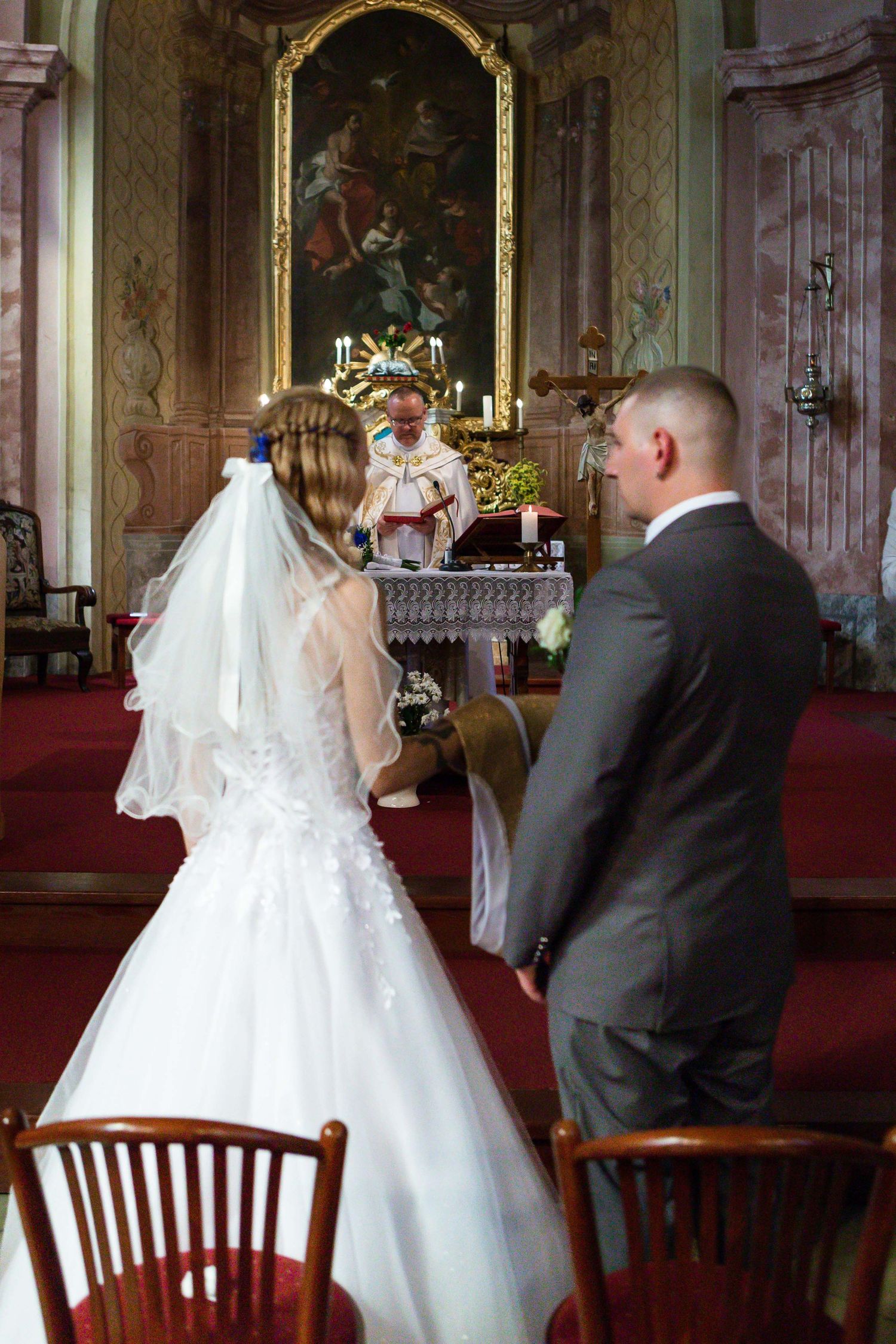 A wedding ceremony takes place inside an ornate church with a couple standing before the altar in traditional attire.