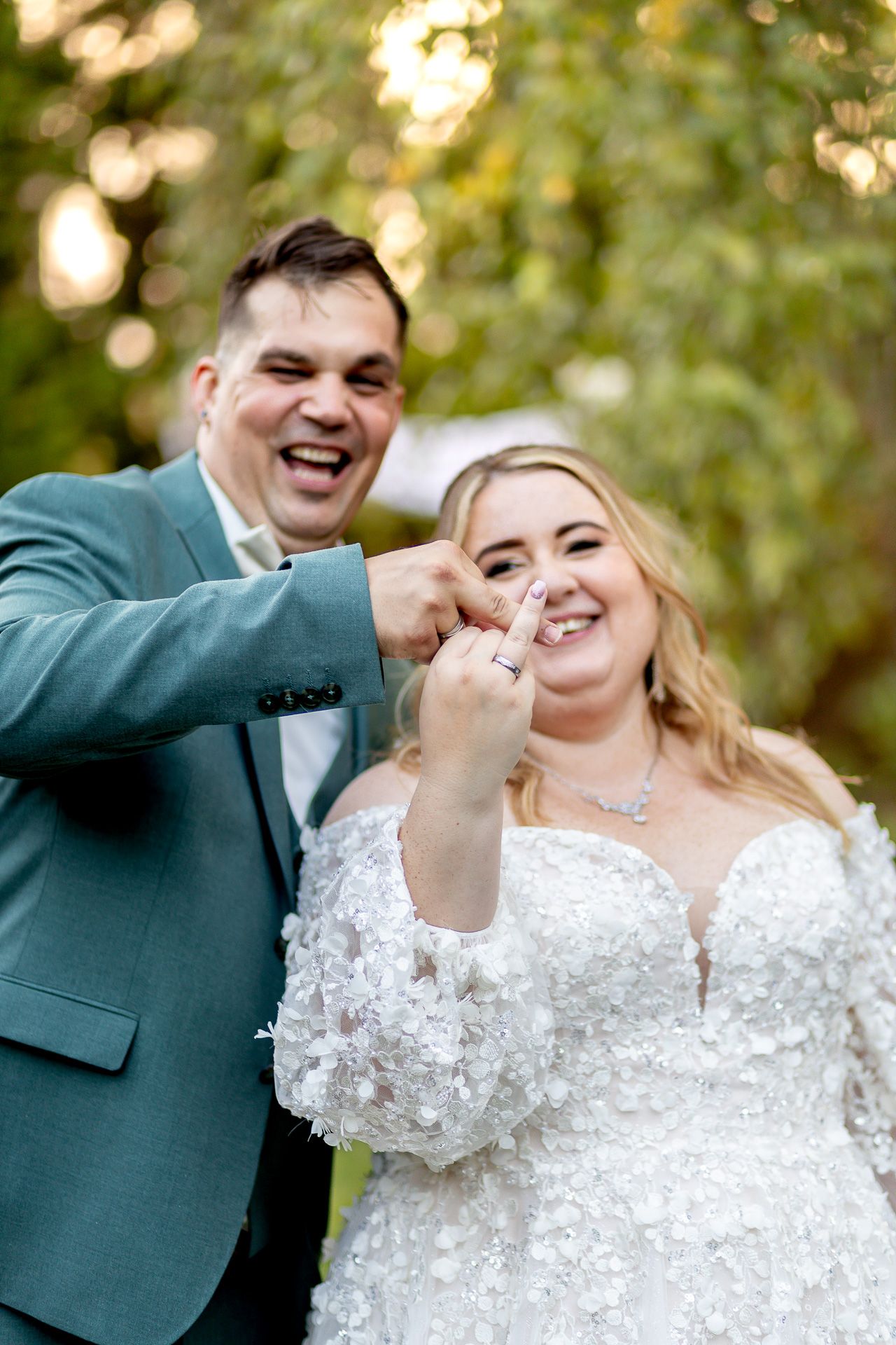 A joyful couple shares a playful moment during their wedding photoshoot in a sunlit outdoor setting.