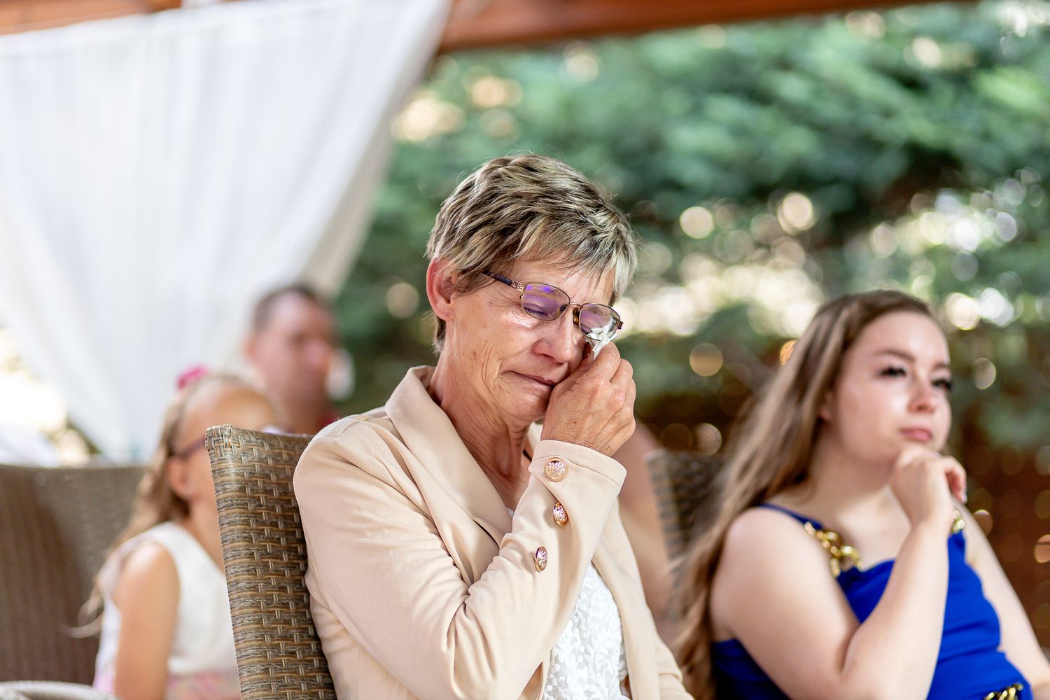 An emotional moment captured during an outdoor wedding ceremony with guests seated beneath white fabric draping.