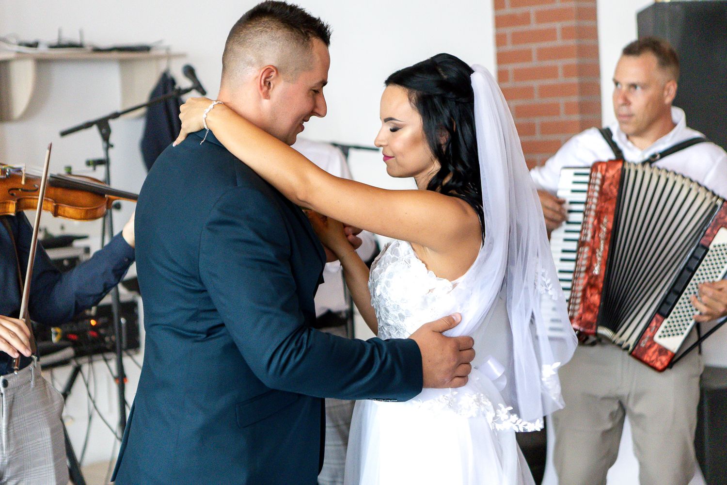 A couple dances together at a wedding celebration while an accordion player performs in the background.
