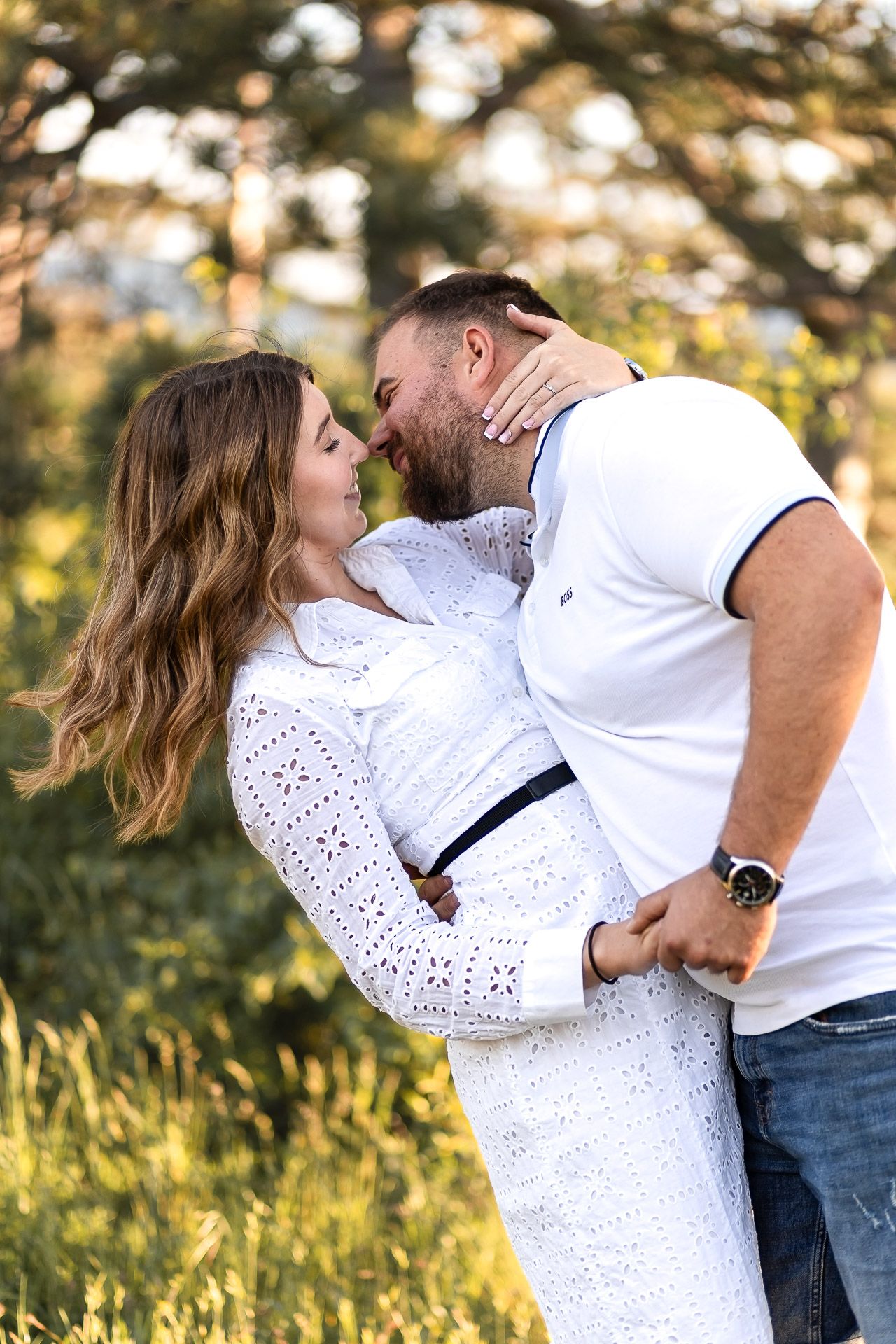 Playful couple in white clothing embraces on mountainside during sunset.