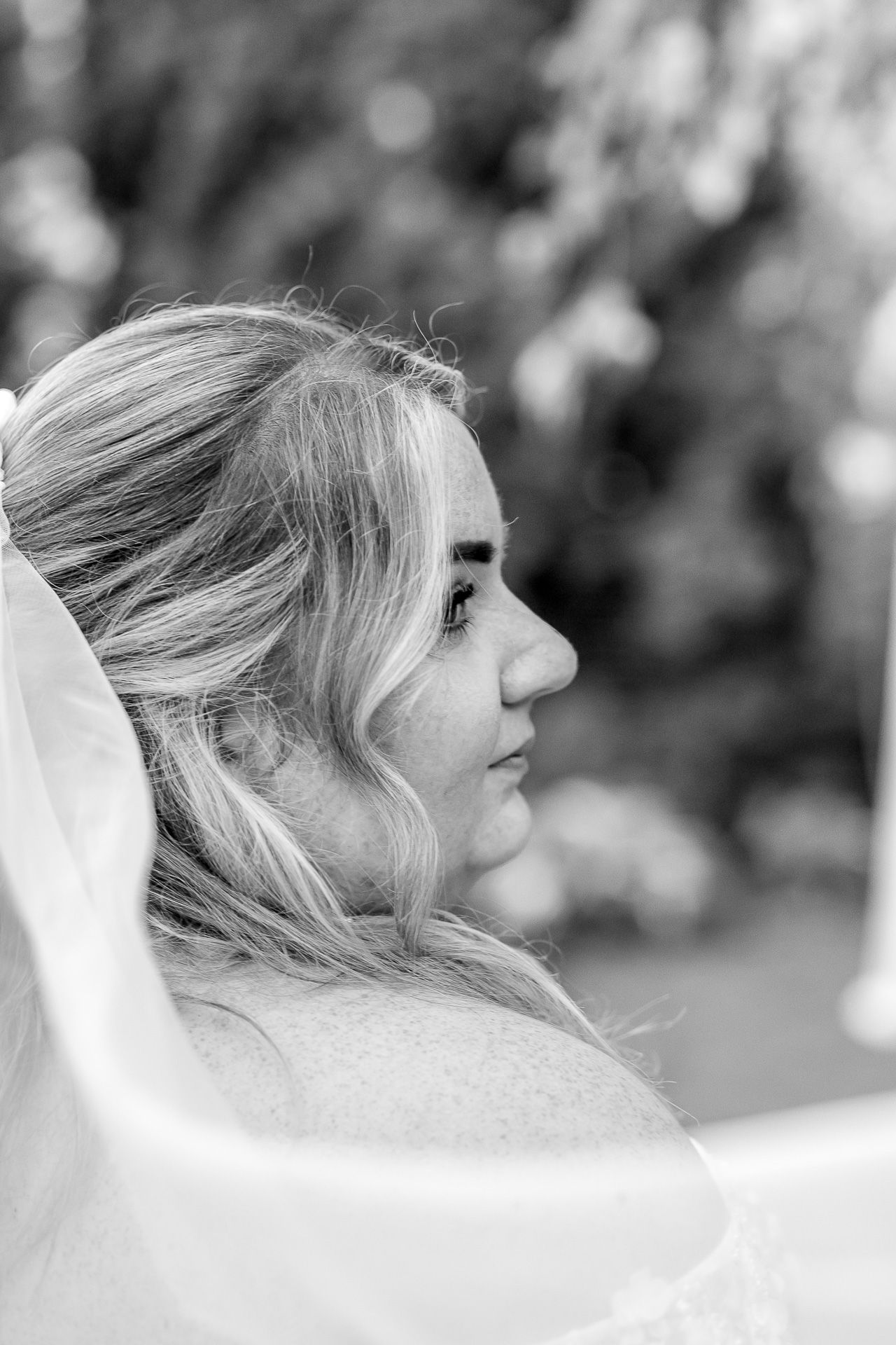 A black and white profile portrait of someone wearing a bridal veil with soft bokeh background.