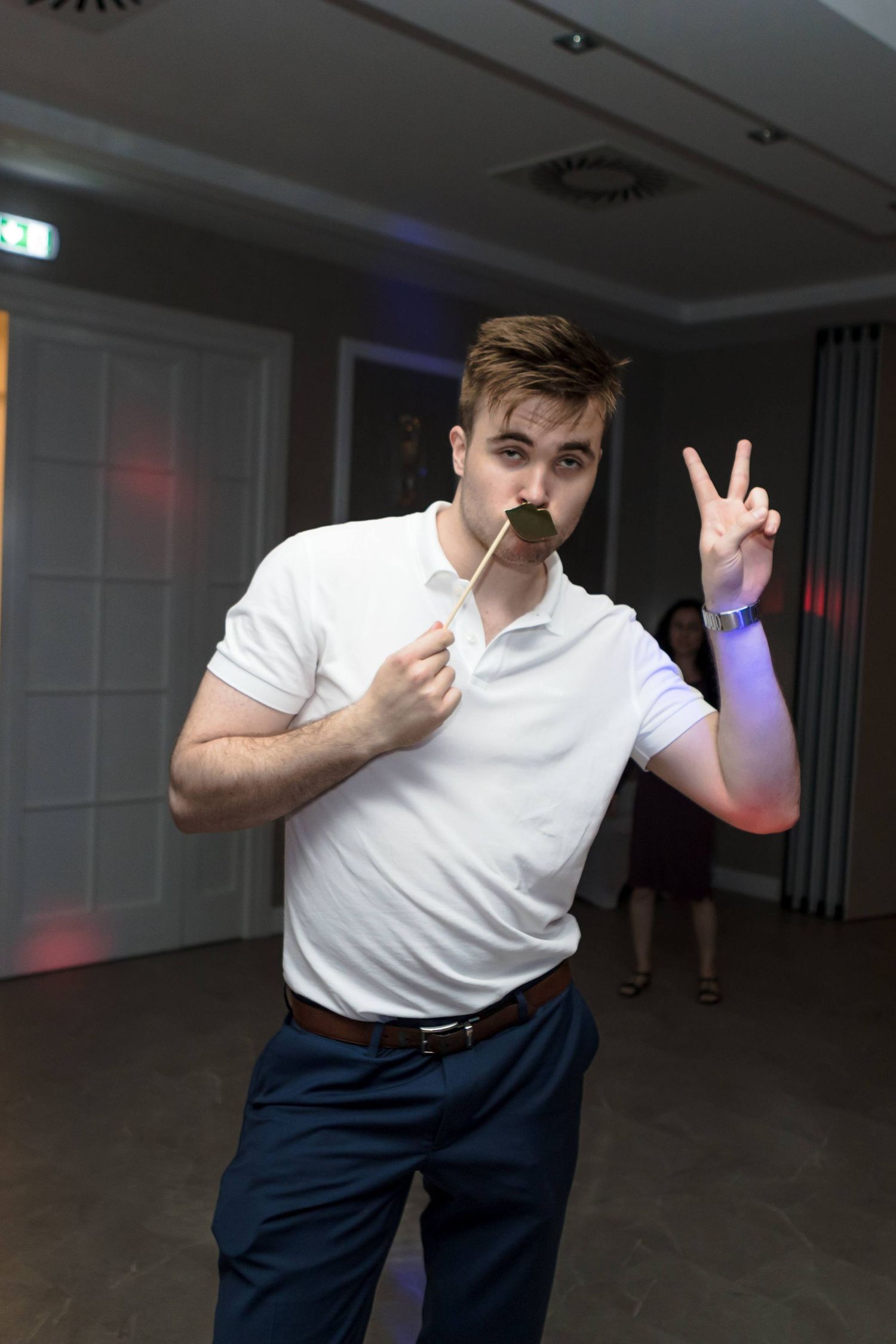 A person in a white t-shirt and dark pants makes dance moves in a dimly lit room with colored lighting.